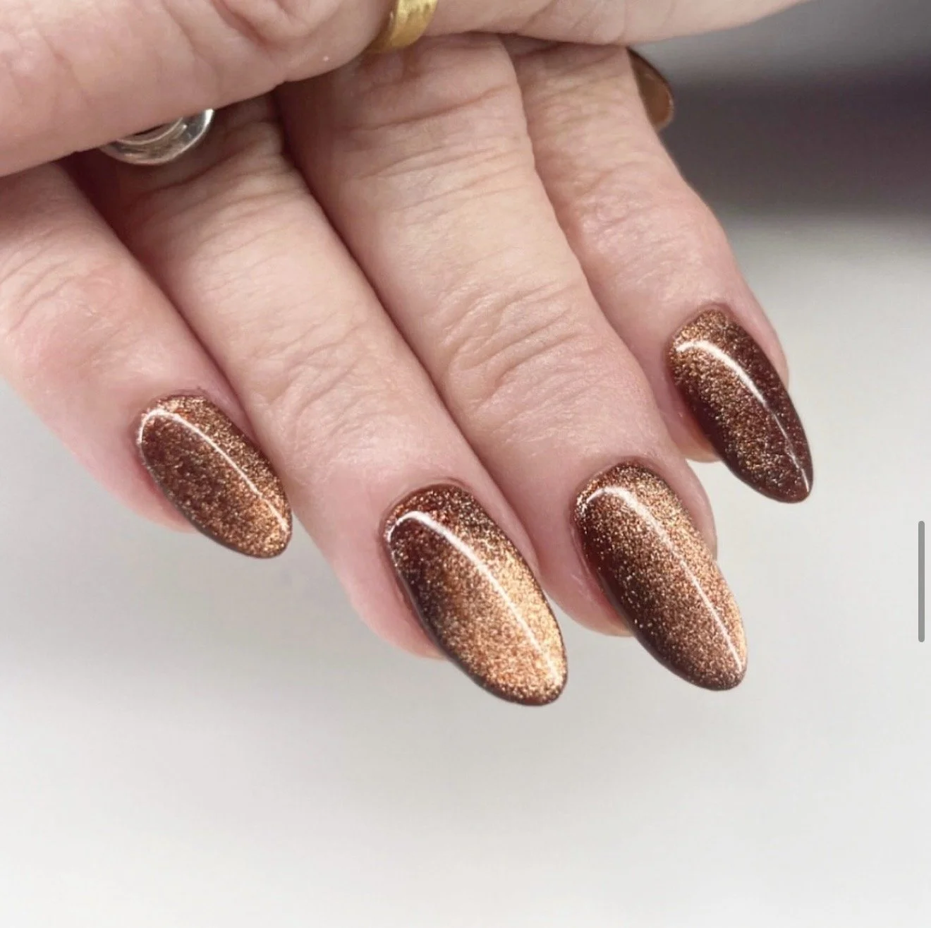 Close-up of a hand with metallic bronze glitter nail polish on almond-shaped nails.