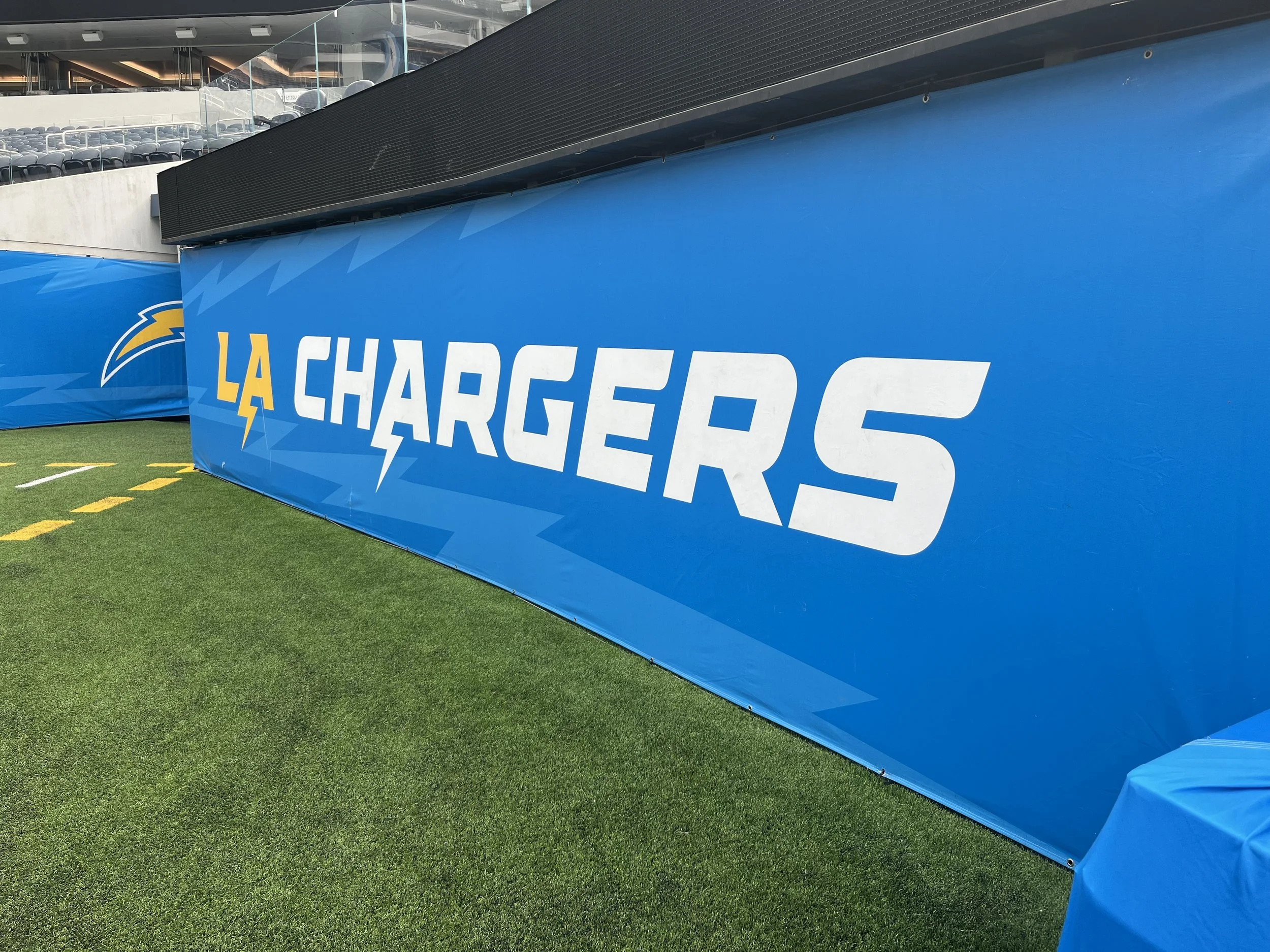 A blue banner with the text 'LA CHARGERS' and a lightning bolt logo, located at Sofi Stadium in Inglewood, CA.