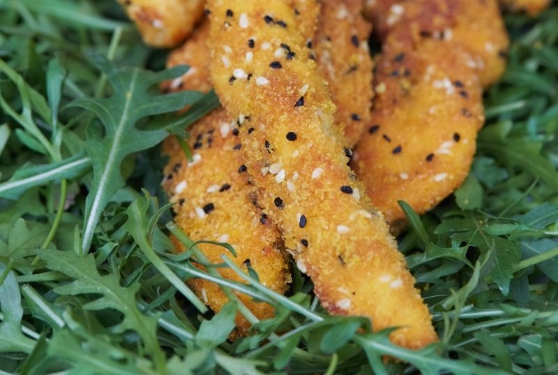 Sprøde kyllingstykker med sesam, serveret på en bund af rucola – smagfuldt og hjemmelavet catering fra Fika.