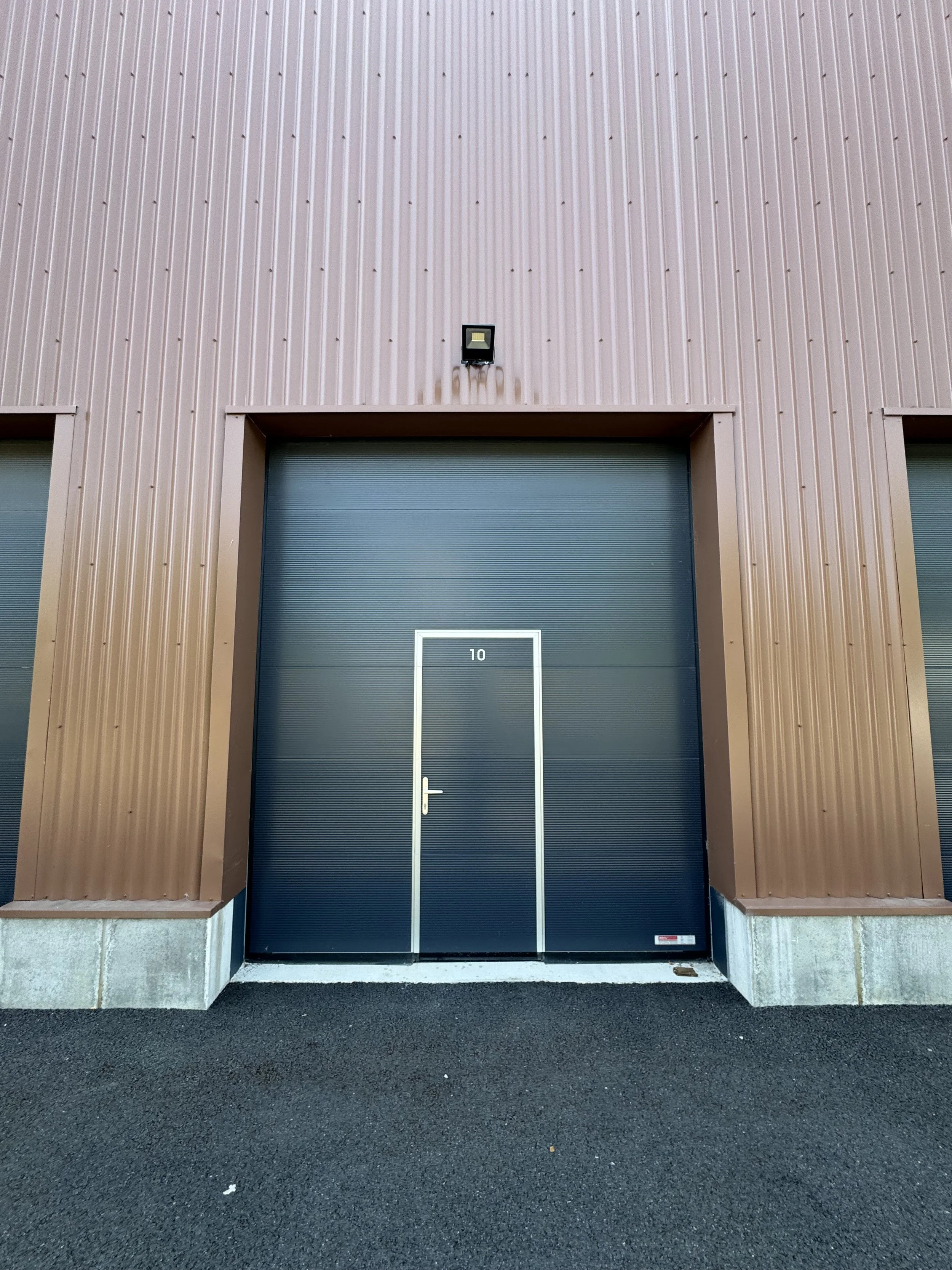 Photo d'une grande porte de garage bleue avec un cadre blanc, numérotée 10, sur un bâtiment en métal brun avec un éclairage au-dessus. A Bailly-Romainvilliers.