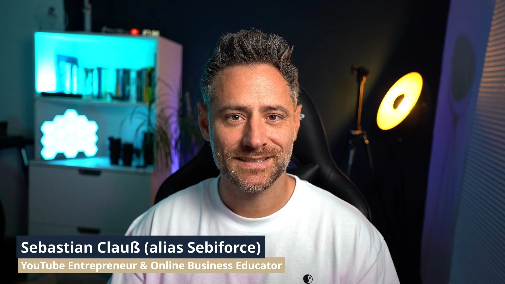 A man with short hair and a beard smiling at the camera in a room with colorful lighting, a bookshelf, and a yellow studio light. Text overlay identifies him as Sebastian Claus, a YouTube entrepreneur and online business educator.