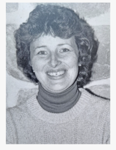 Black and white photo of a woman with curly hair, smiling, wearing a turtleneck sweater.