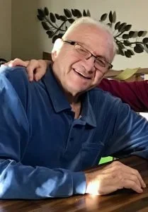 Smiling elderly man with glasses sitting at a table.