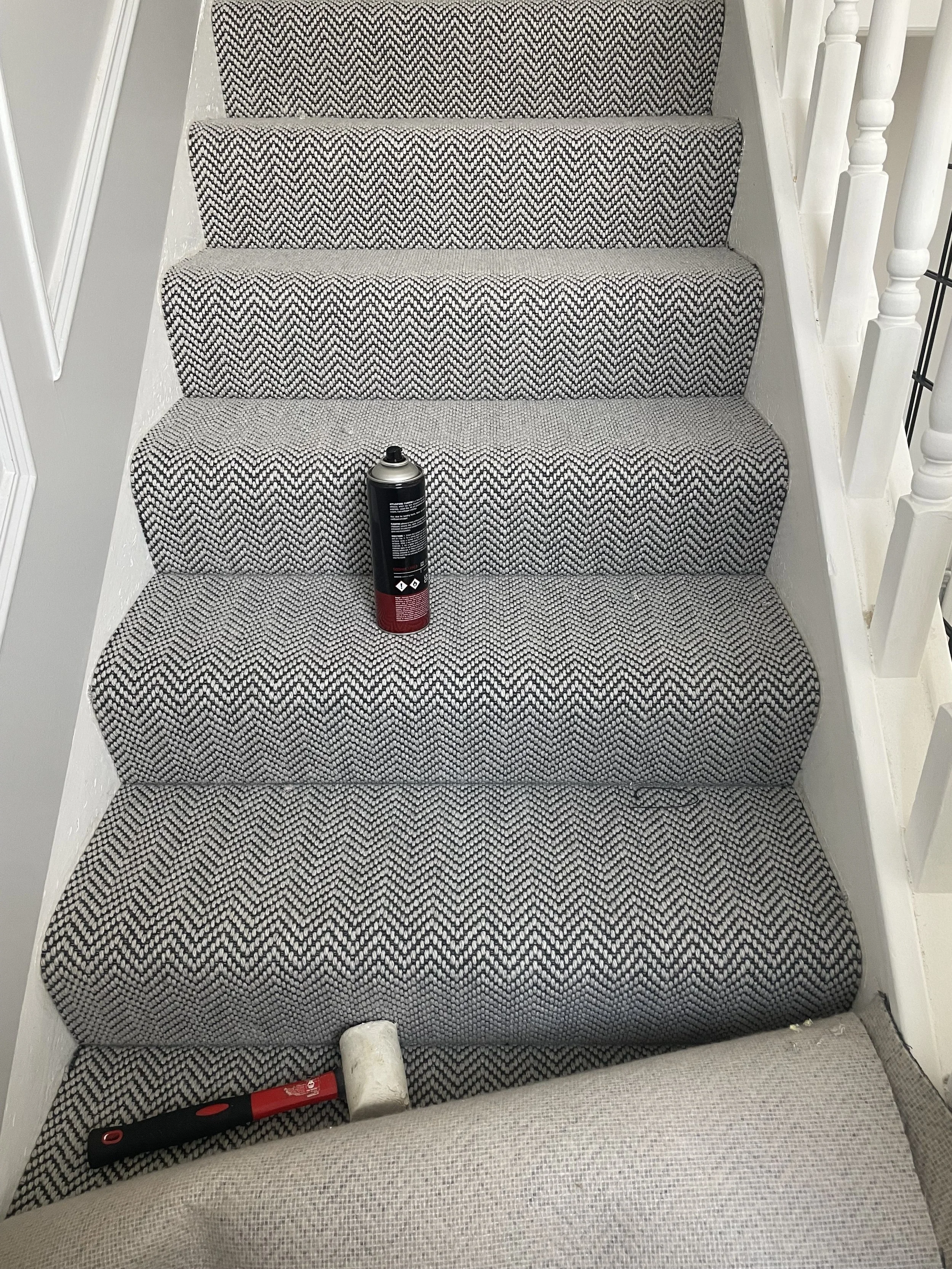 Staircase with black and white zigzag patterned carpet, a can of spray foam, a small white foam block, and a hammer lying on the stairs.