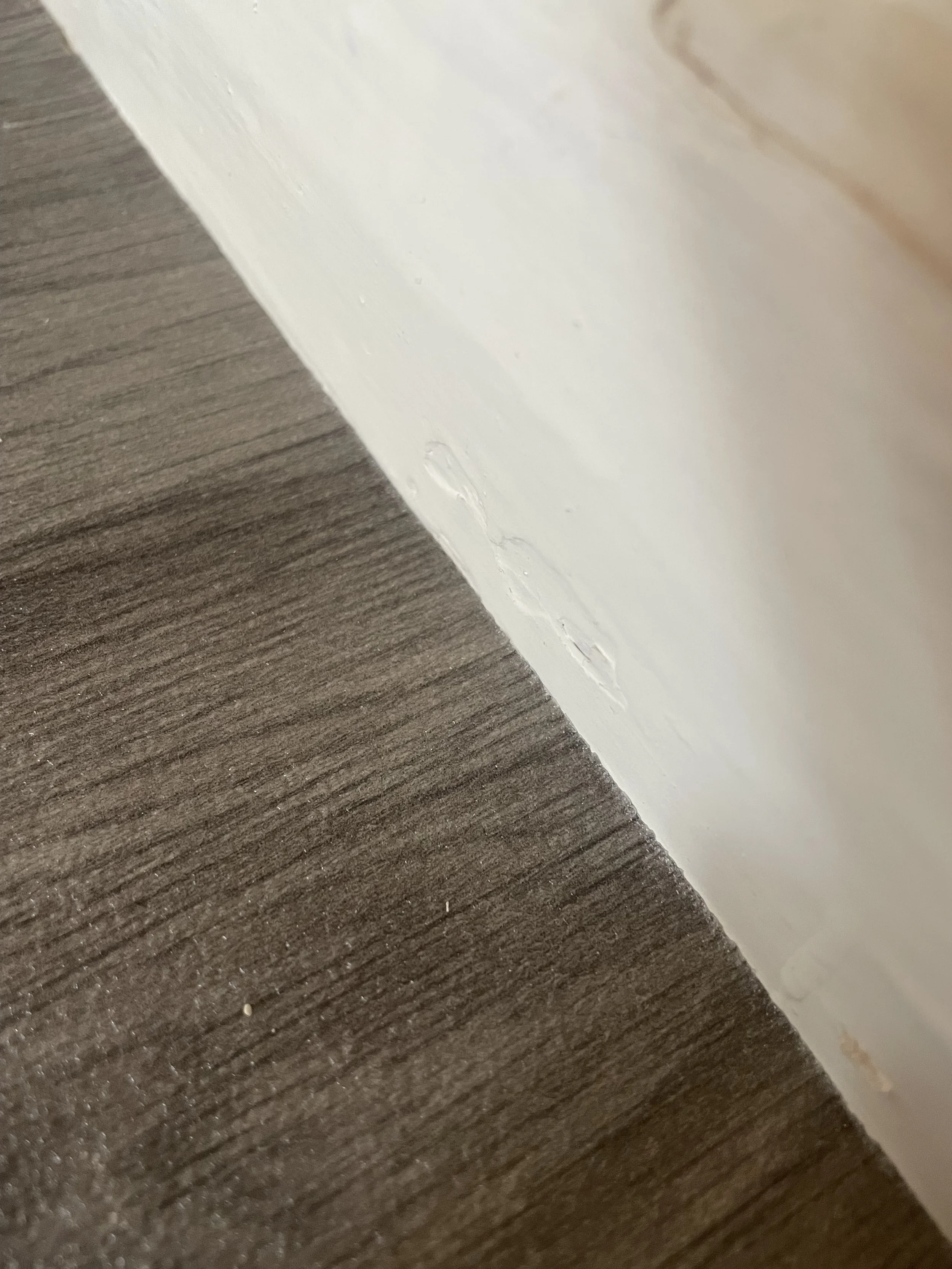 Close-up of a white painted wall meeting a dark wooden floor, with visible scuff marks and dirt near the baseboard.