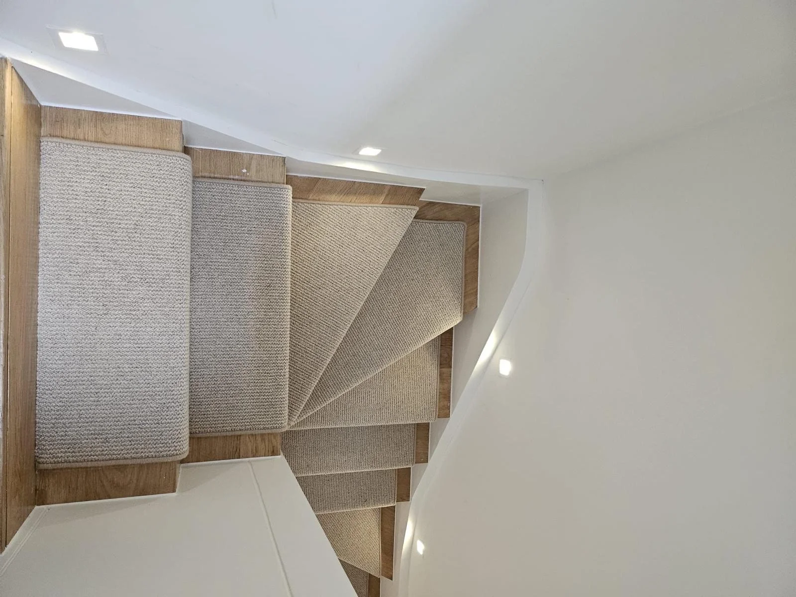 Carpeted staircase with wooden steps and white walls.