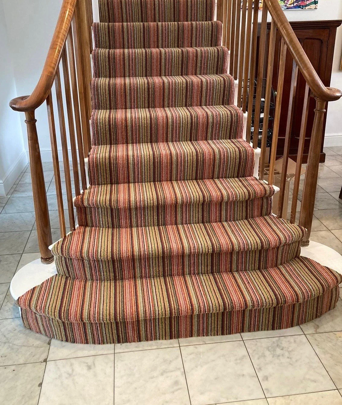 Staircase with a colorful striped carpet and wooden railing inside a home.