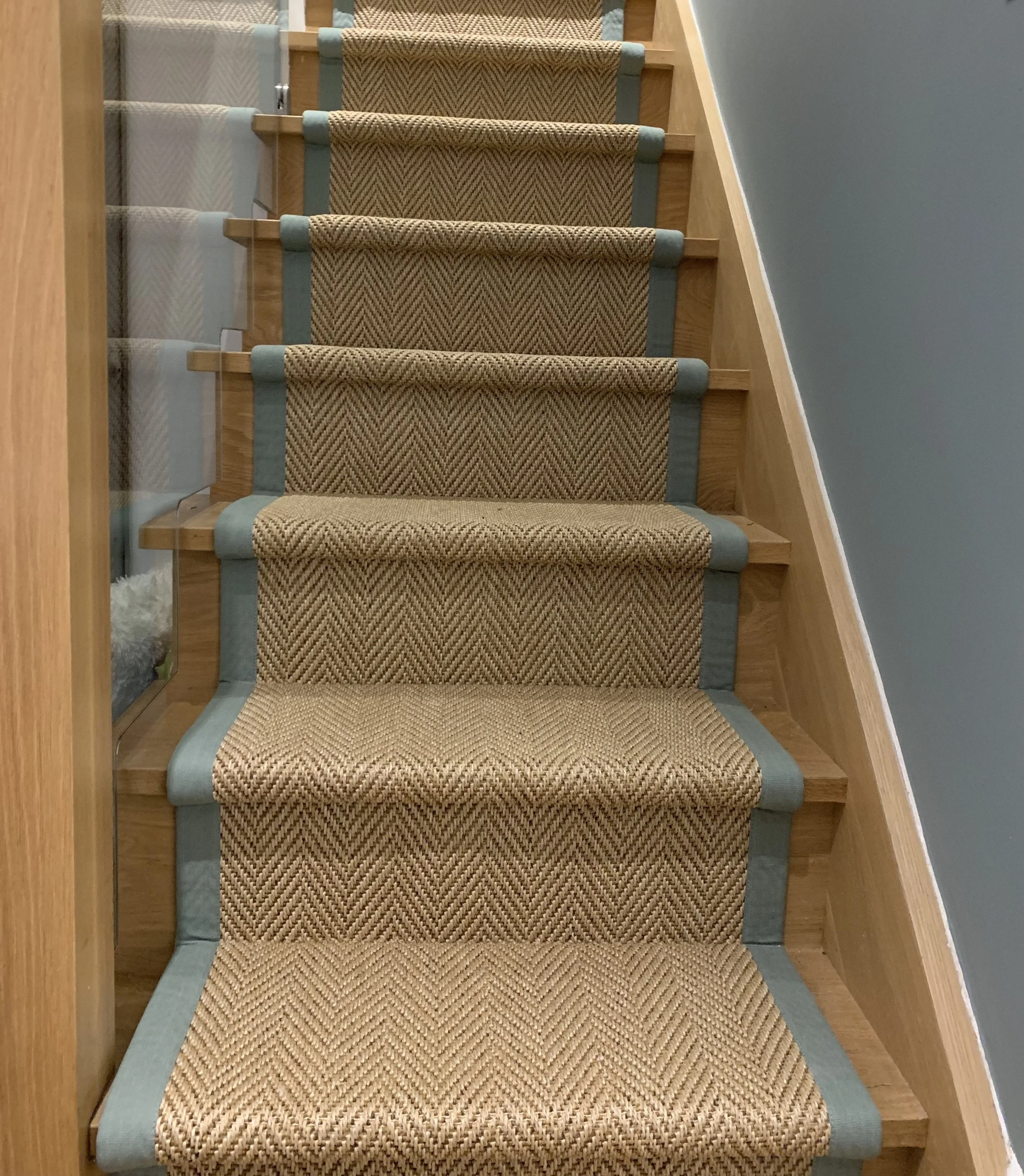 Carpeted staircase with beige and blue patterned runner, wooden stairs, and light blue wall with wooden trim.