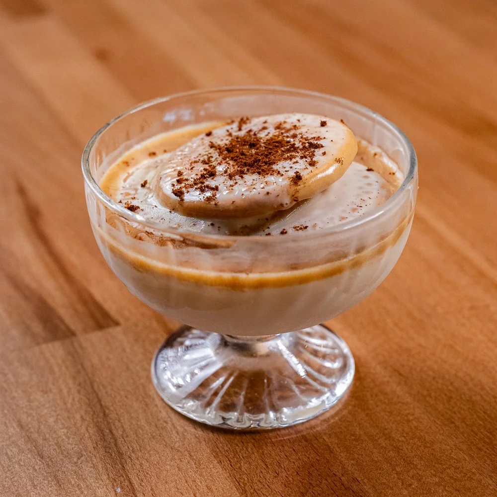 dessert in a glass bowl with a banana slice and sprinkled cinnamon on top