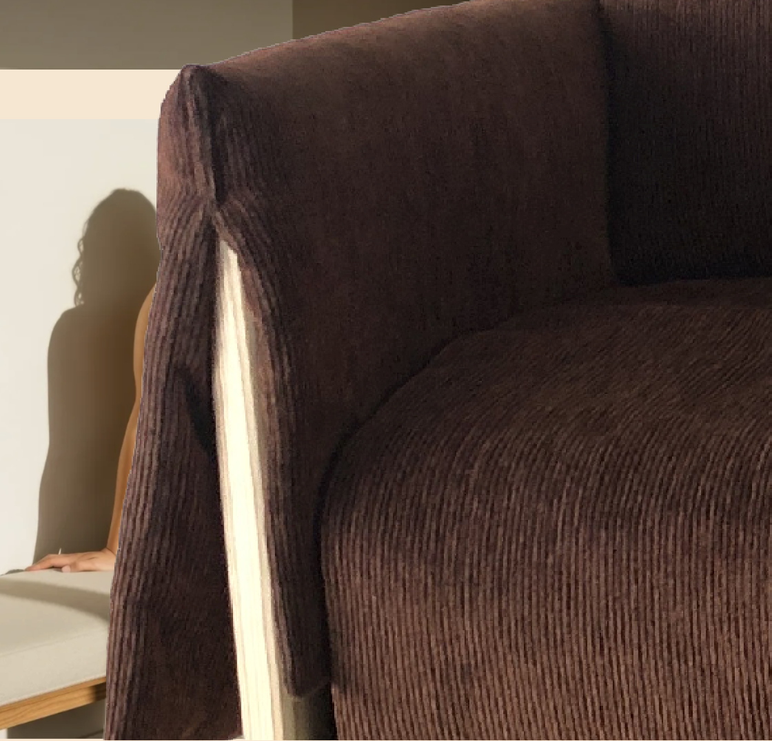 A person with curly hair sitting on a white chair, partially obscured behind a large brown upholstered armchair.
