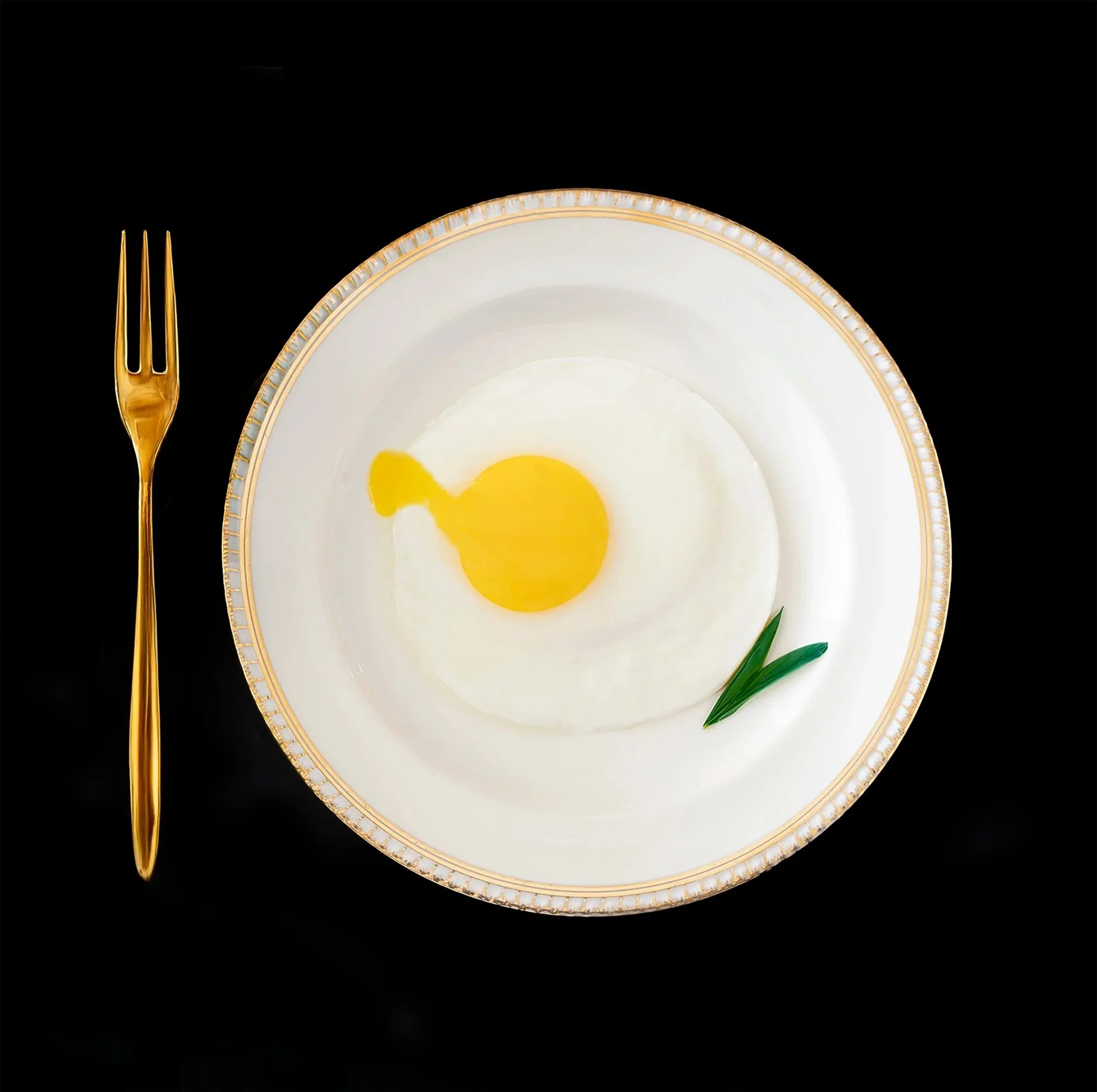 minimist still life of a white plate with a yellow egg shape and gold fork on black background