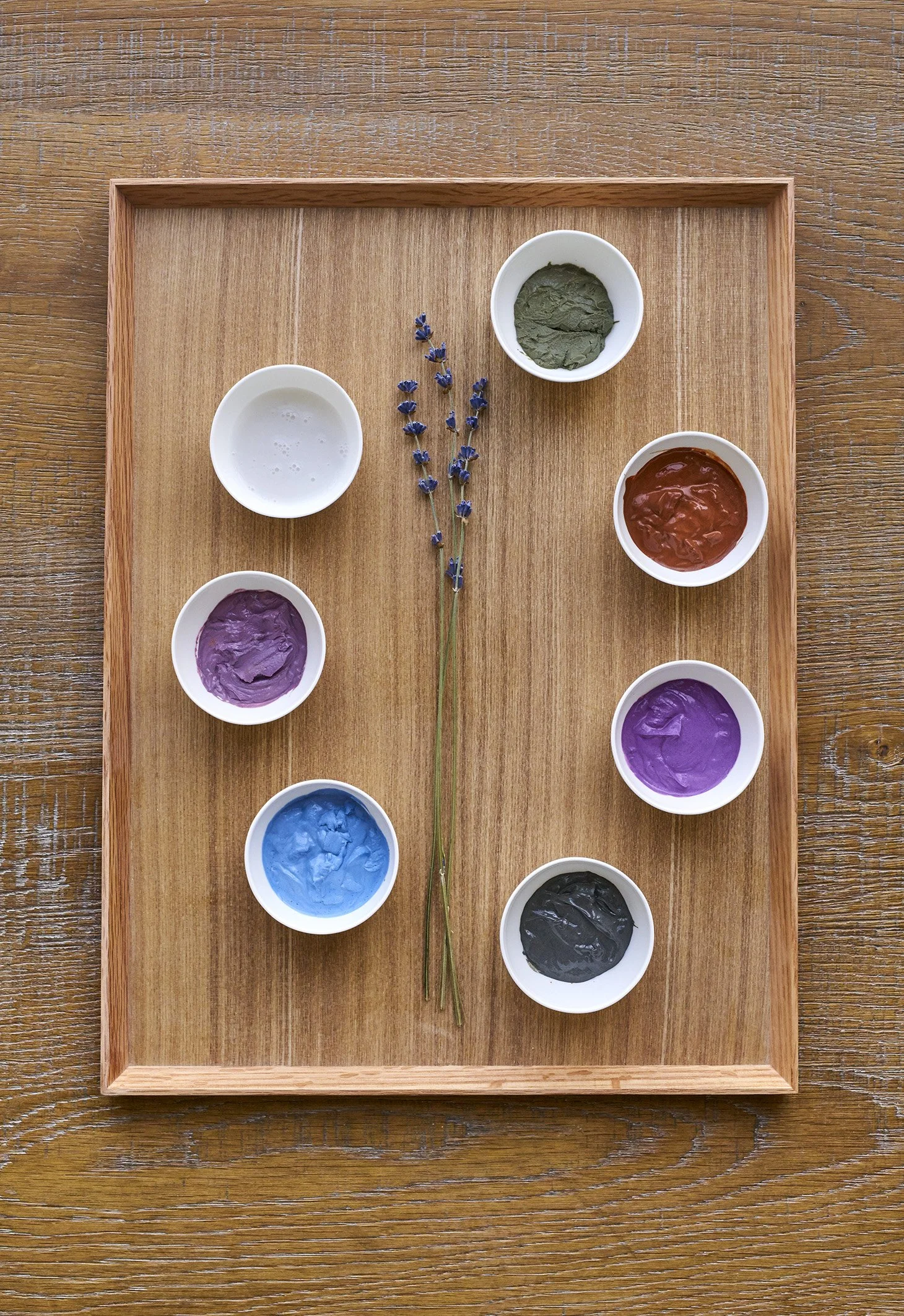 Bunte Farben in kleinen Schalen auf einem Holztablett, mit Lavendel in der Mitte.