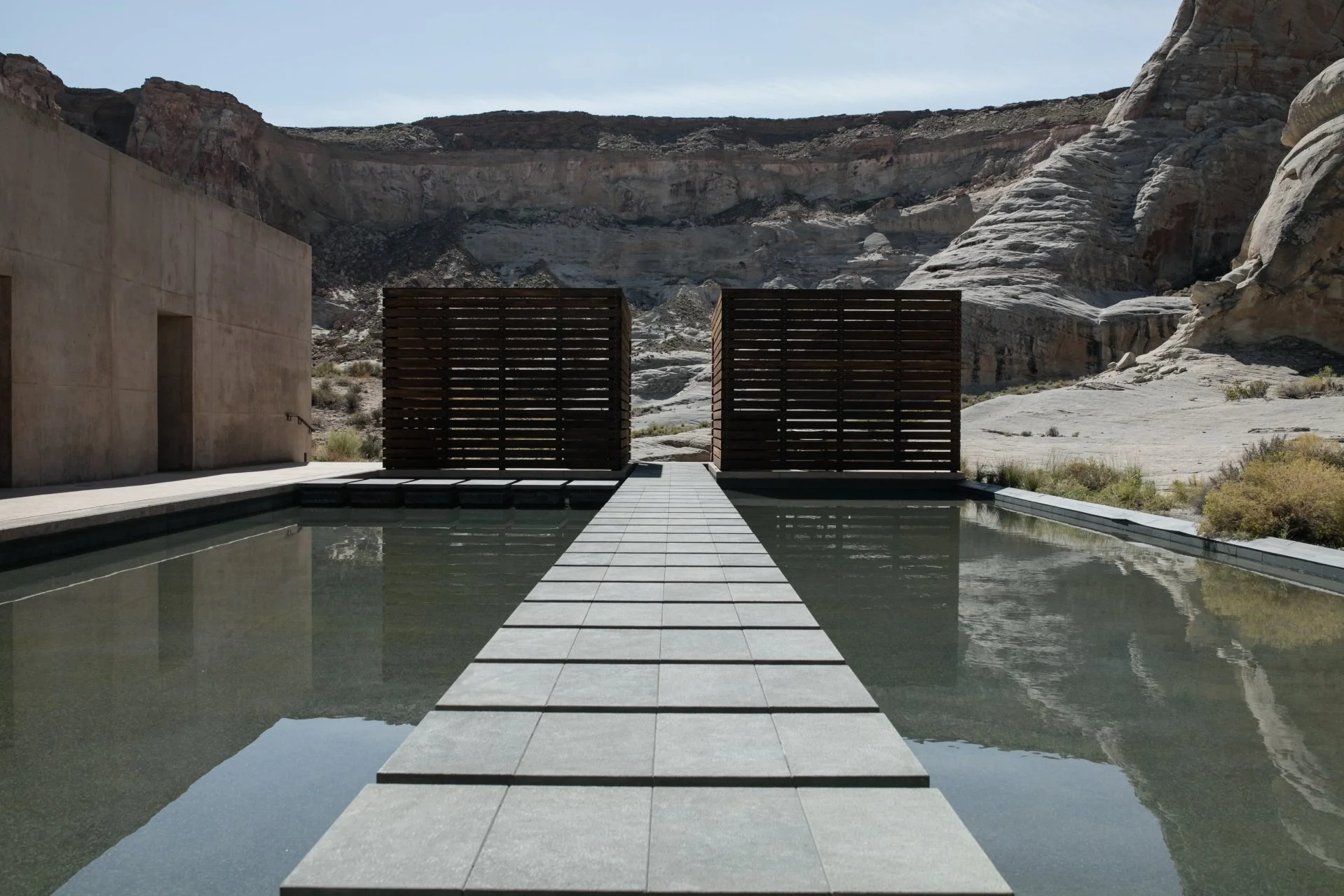Moderne, minimalistische Poolanlage mit überdachtem Pavillon vor einem Wüsten- oder Berglandschaft im Hintergrund.