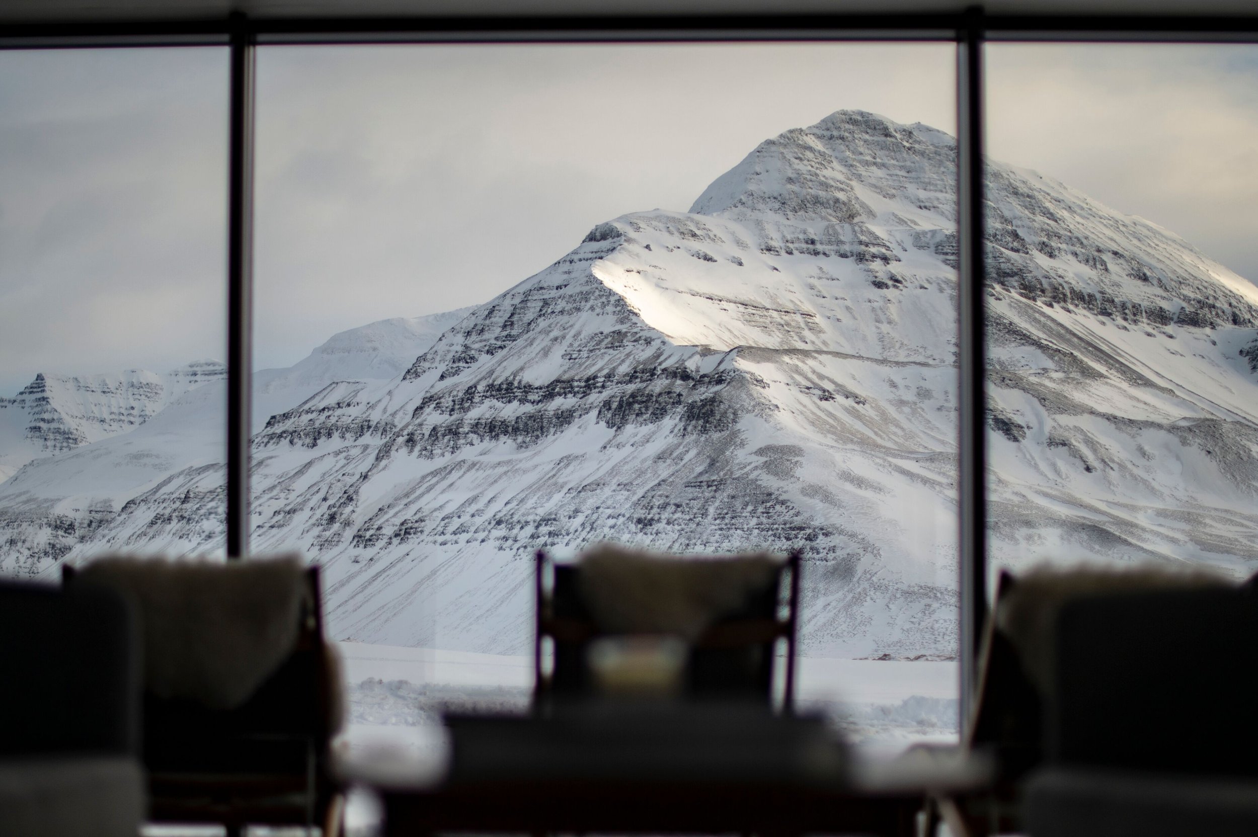 Innenaufnahme mit Blick auf schneebedeckte Berge durch großes Fenster, im Vordergrund Möbel