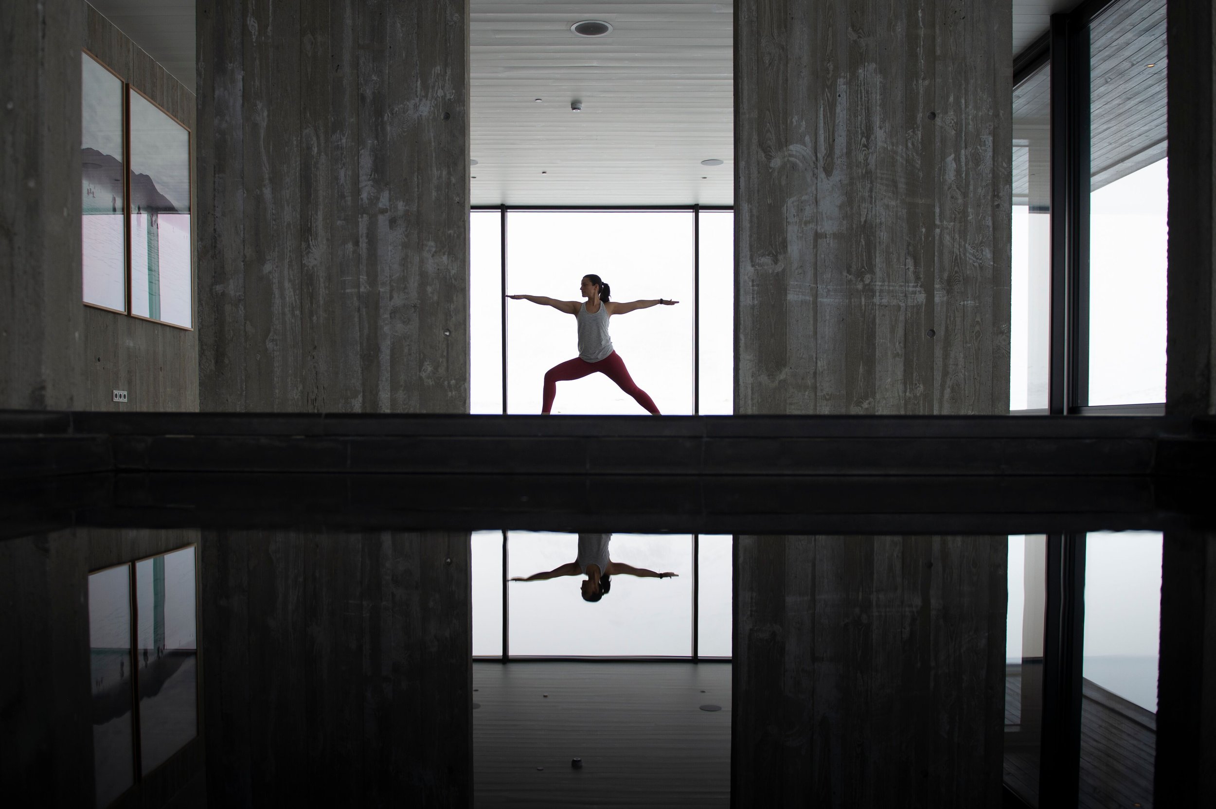 Frau beim Yoga in einem modernen Raum, die Yoga-Position im Lotos mit ausgestreckten Armen, mit Reflexion im Wasser