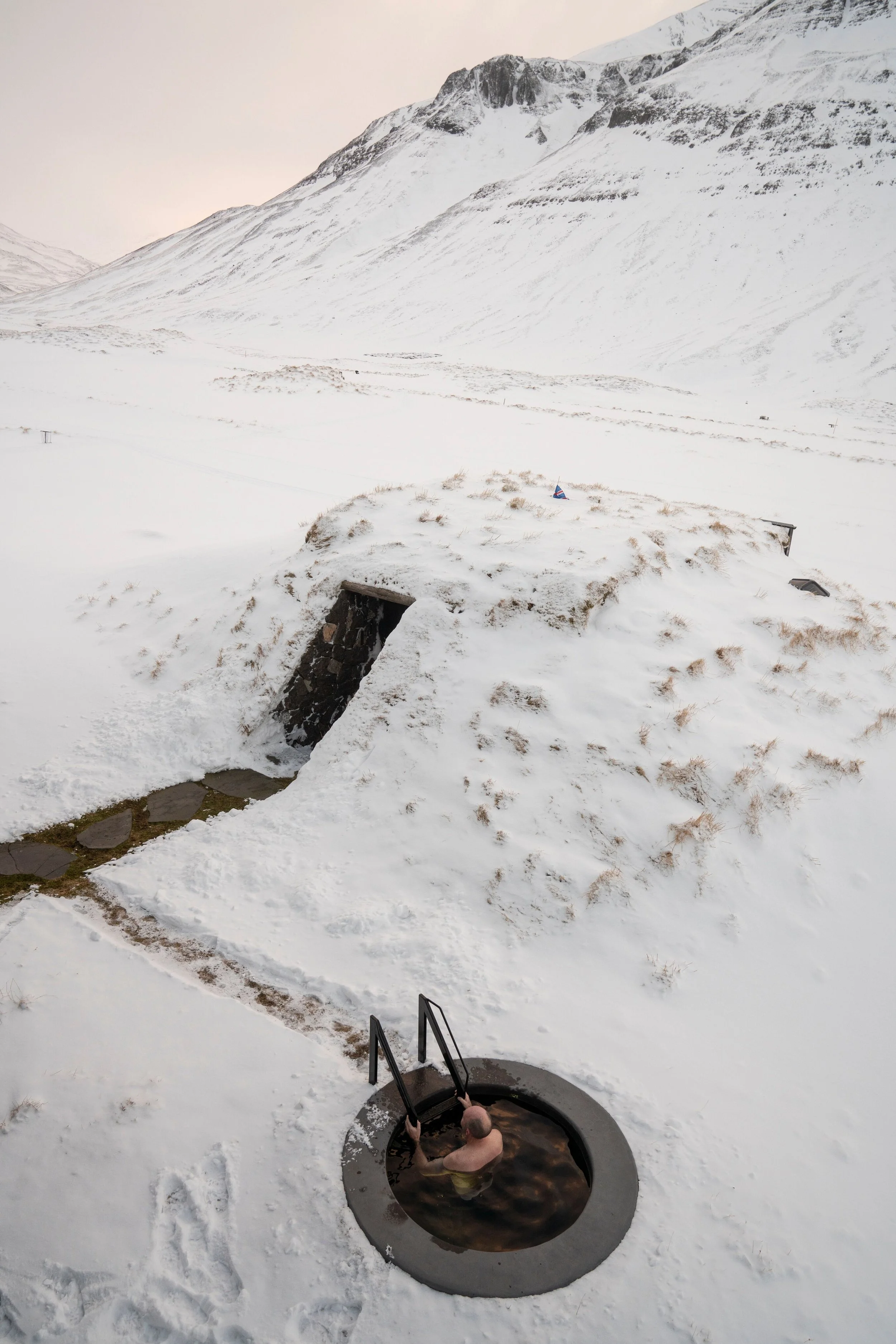 Ein Mann badet in einem hot tub im Schnee in einer schneebedeckten Berglandschaft.