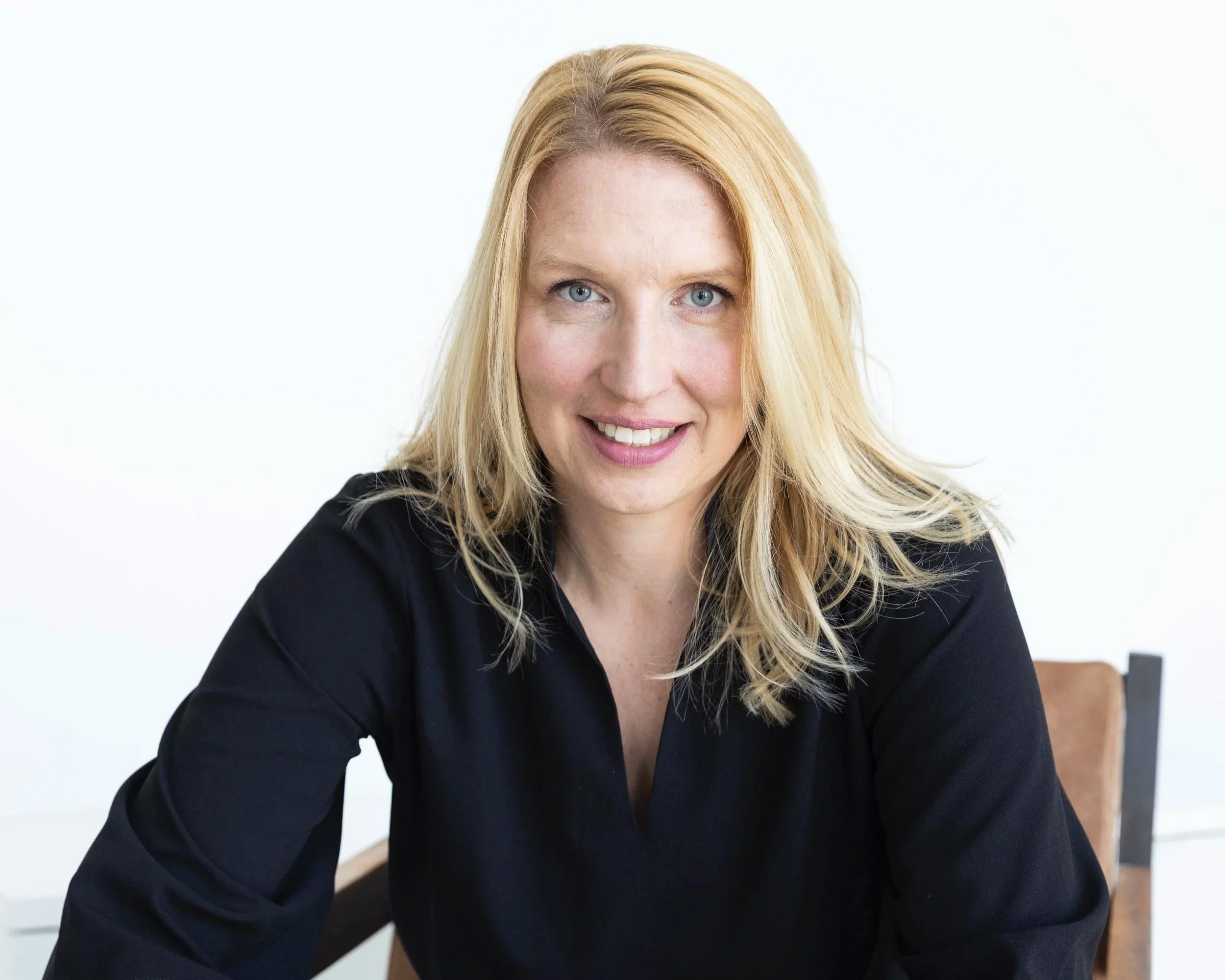 Eine blonde Frau in schwarzem Hemd sitzt an einem Tisch vor white Hintergrund.