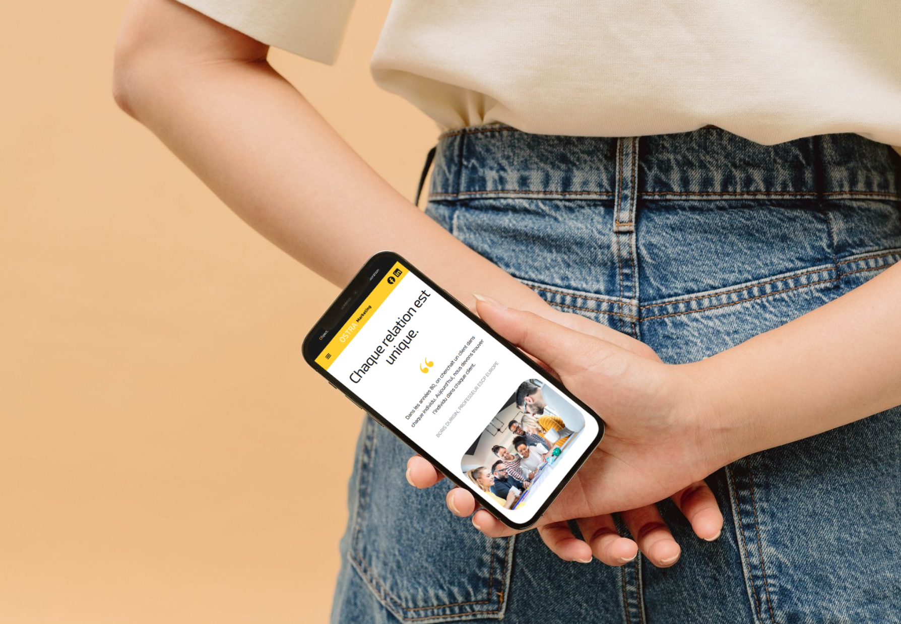 Person tenant un smartphone montrant une page web avec un texte en français et une image de plusieurs personnes souriantes autour d'une table, dans un environnement intérieur.
