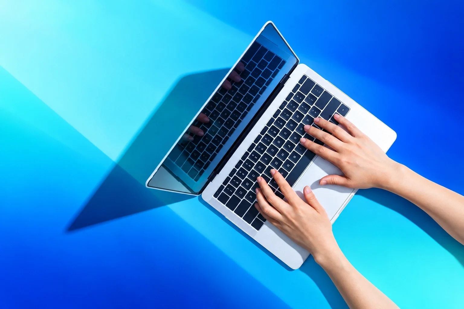 Mains d'une personne tapant sur un clavier d'ordinateur portable sur une surface bleue