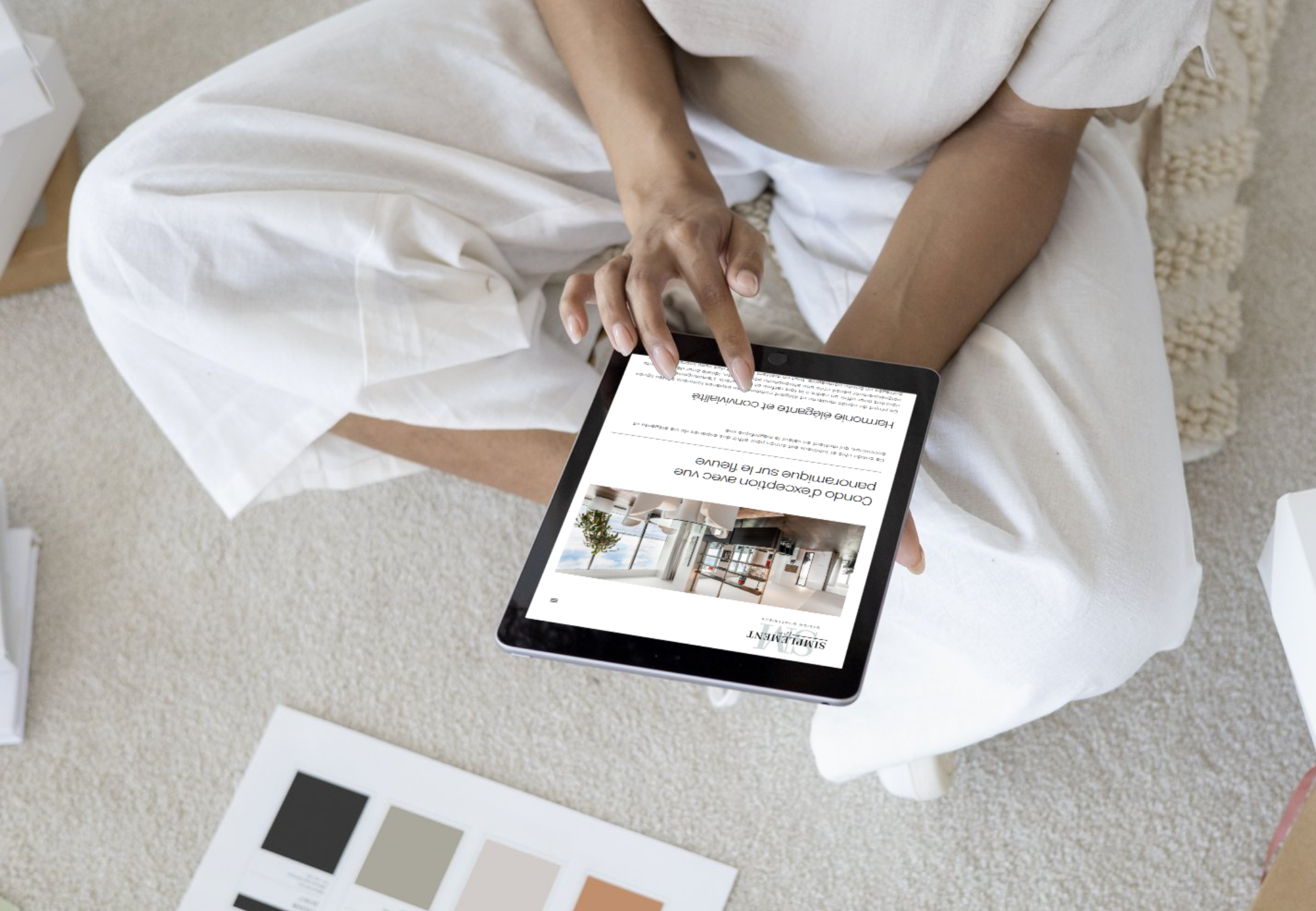 Personne assise sur un canapé blanc, utilisant une tablette pour lire une image et un texte à propos d'un appartement moderne et lumineux.