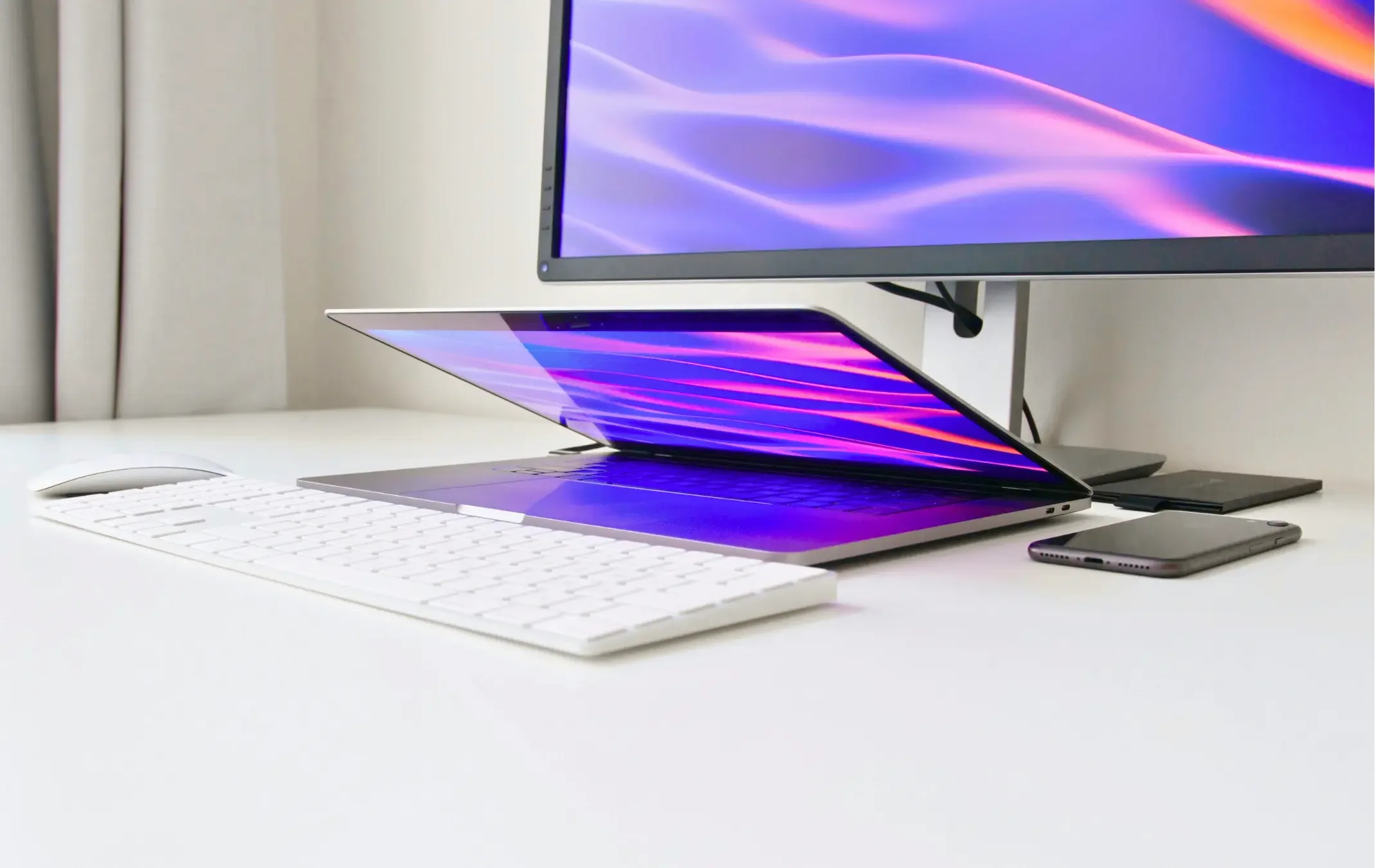 Un ordinateur portable, un clavier sans fil, une souris, un smartphone et deux écrans connectés dans un bureau blanc.