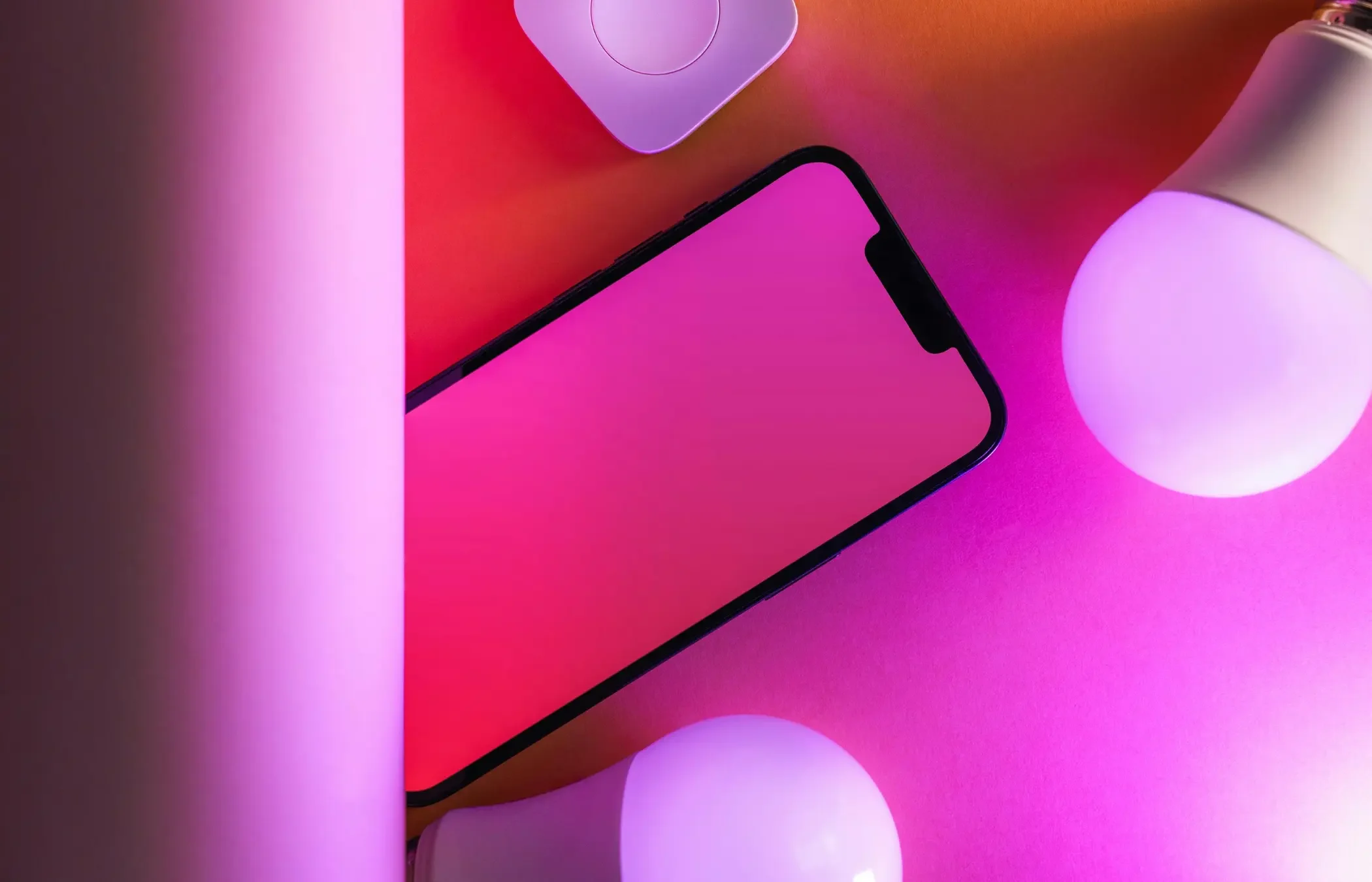 Un téléphone avec un écran noir posé sur une surface rose lumineuse, entouré de boules blanches et de lumières violettes et roses.