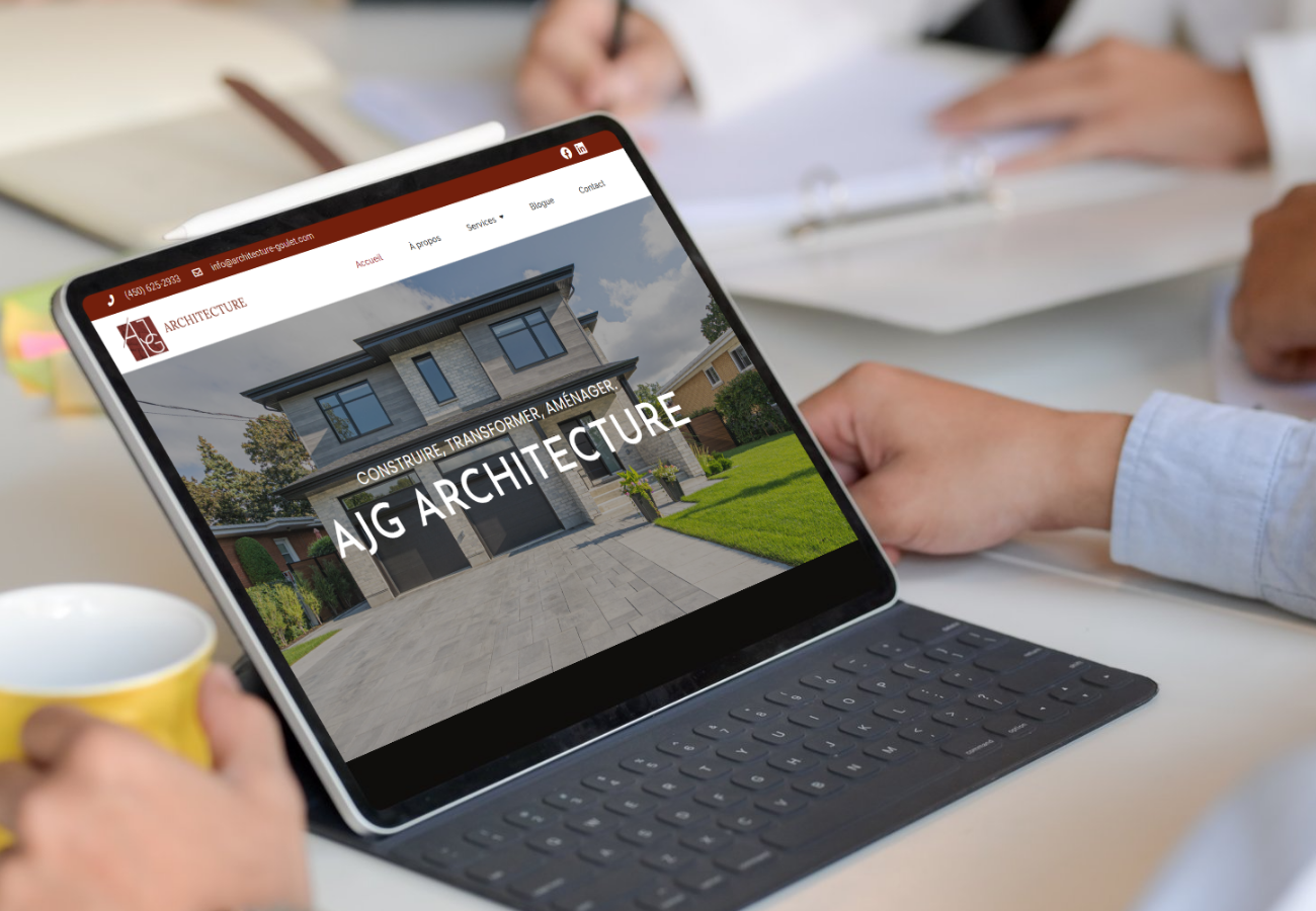 Une personne tenant une tablette affichant le site web d'une entreprise d'architecture AJG Architecture, avec un bâtiment moderne en fond. Autour, il y a d'autres personnes à une réunion, avec des notes et une tasse jaune.
