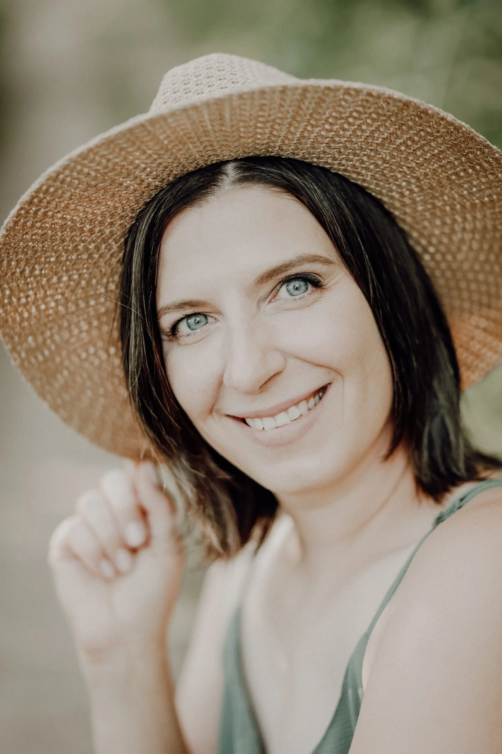 Femme souriante portant un grand chapeau en paille, extérieur, regardant vers l'appareil photo.