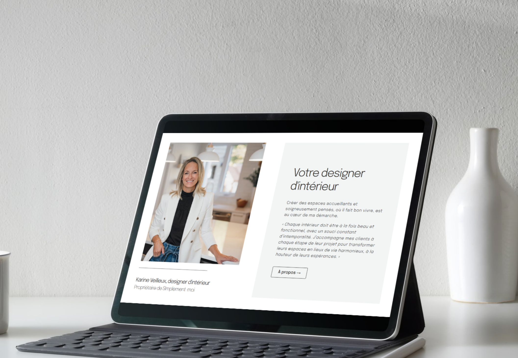 Un ordinateur portable affichant une page web présentant une femme et une description de designer d'intérieur, située sur un bureau avec un vase blanc à droite.