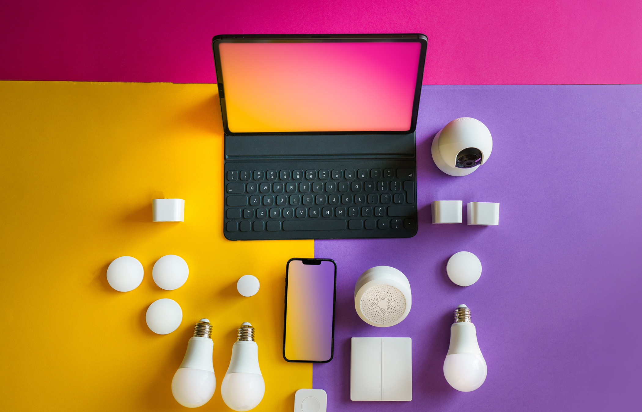 Tableau coloré avec divers objets technologiques et d'éclairage, dont une tablette avec clavier, un téléphone, une caméra, des ampoules, des balles en plastique et des petits appareils, sur un fond jaune et violet