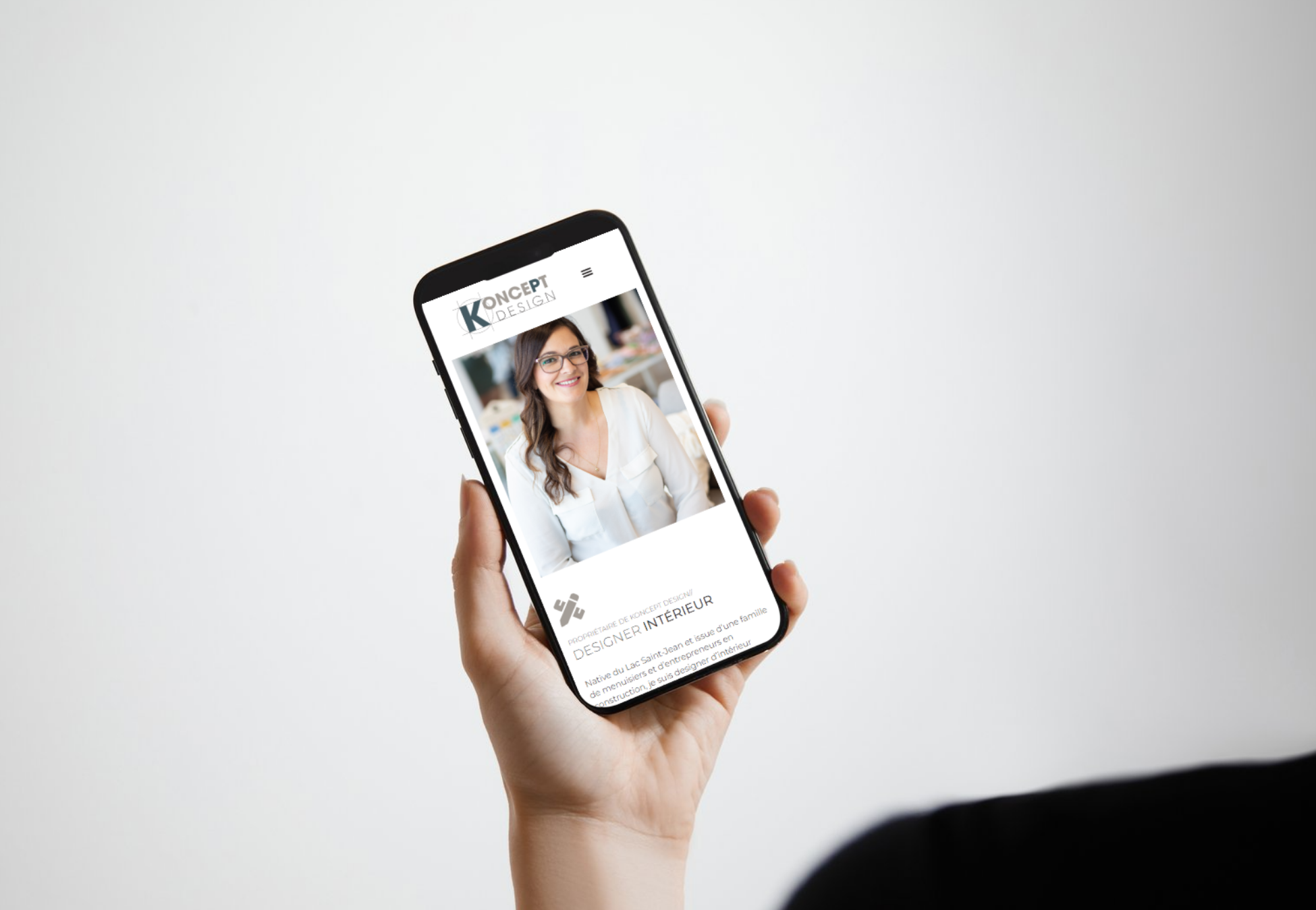 Capture d'écran d'une femme tenant un smartphone affichant un site web de design d'intérieur avec une photo d'une femme souriante portant des lunettes.