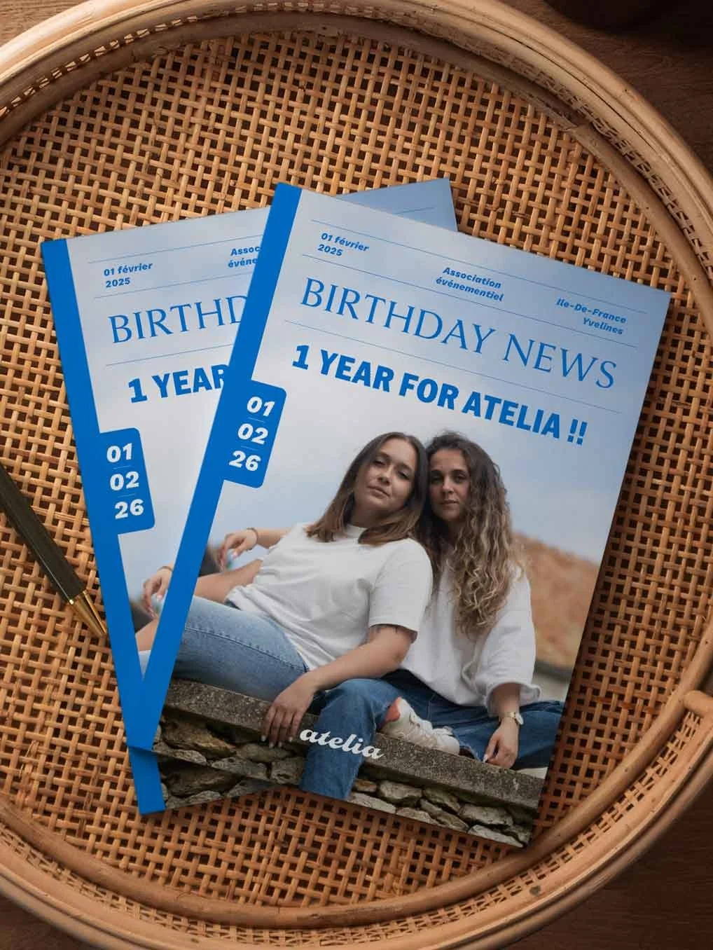 Deux magazines bleu et blanc pour célébrer le premier anniversaire d'Atelia, datés du 1er février 2025, avec une photo de deux jeunes femmes assises sur un mur dans un cadre naturel