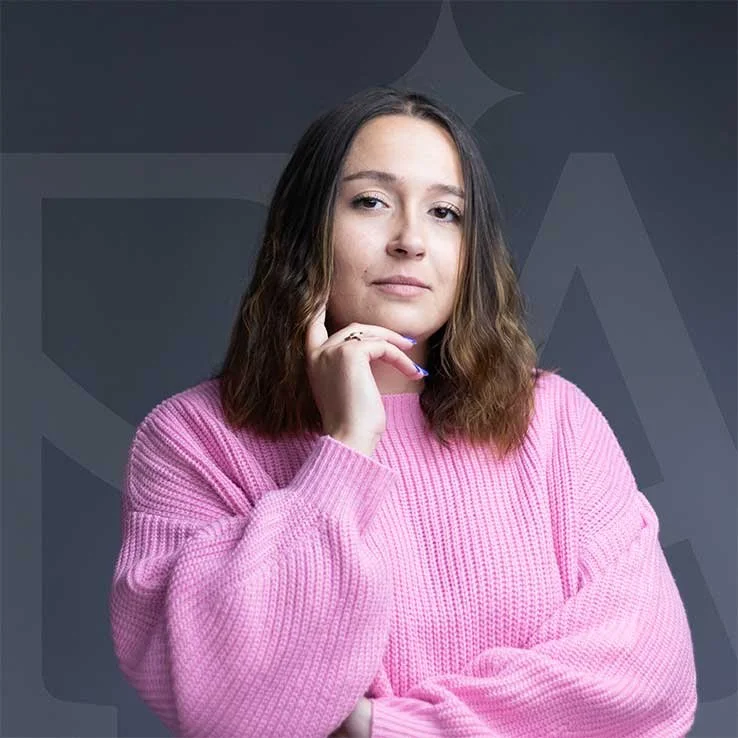 Alicia Rando, fondatrice de Studio Grafalia, portant un pull rose, posant avec la main sous le menton, avec son monogramme en fond