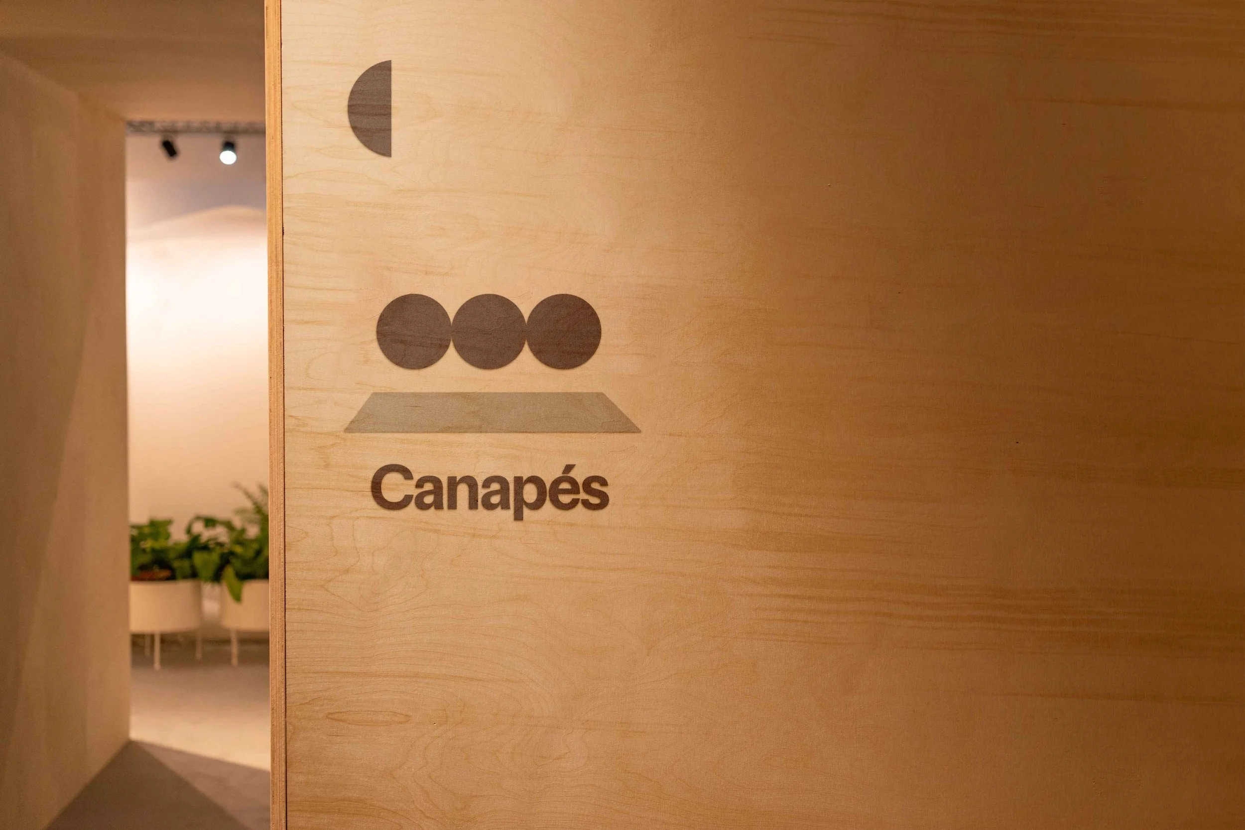 Une signalisation en bois indiquant le nom 'Canapés' dans un intérieur d'espace de design moderne, avec des plantes vertes en arrière-plan (magasin de décoration)