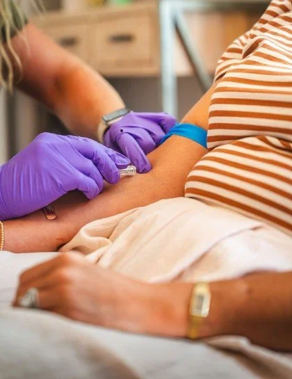 A person in a striped shirt receiving a vaccination in their upper arm from a healthcare worker wearing purple gloves.