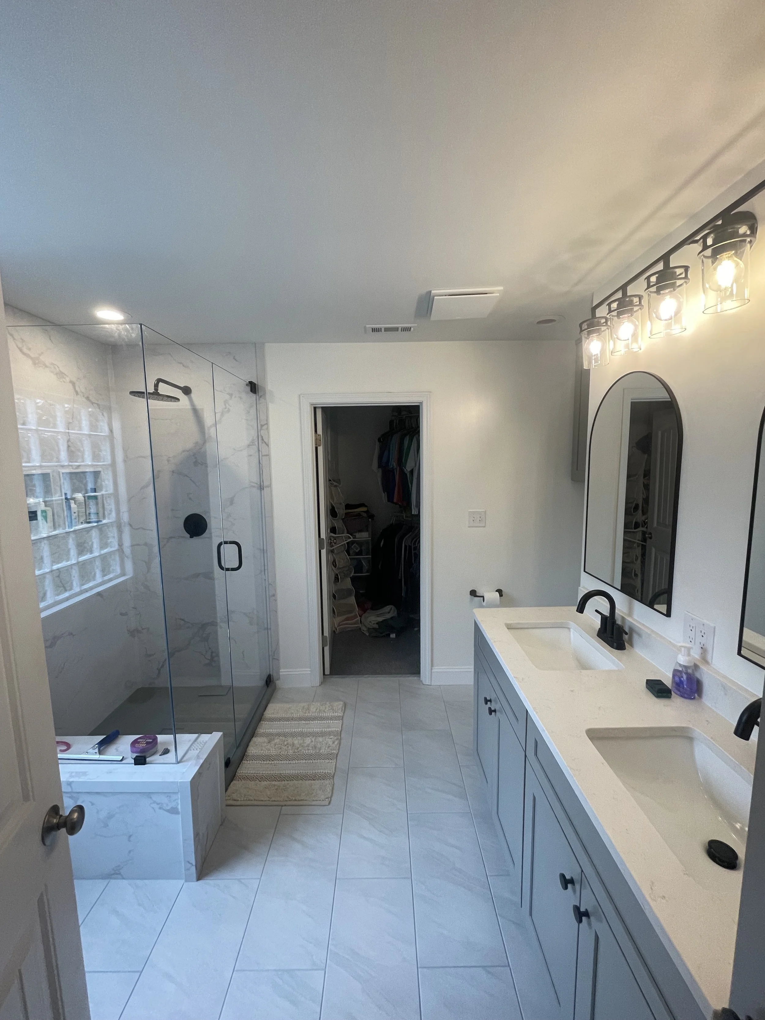 Bathroom with walk-in shower, two mirrors above a blue vanity with cream countertop, and laundry closet in the background.