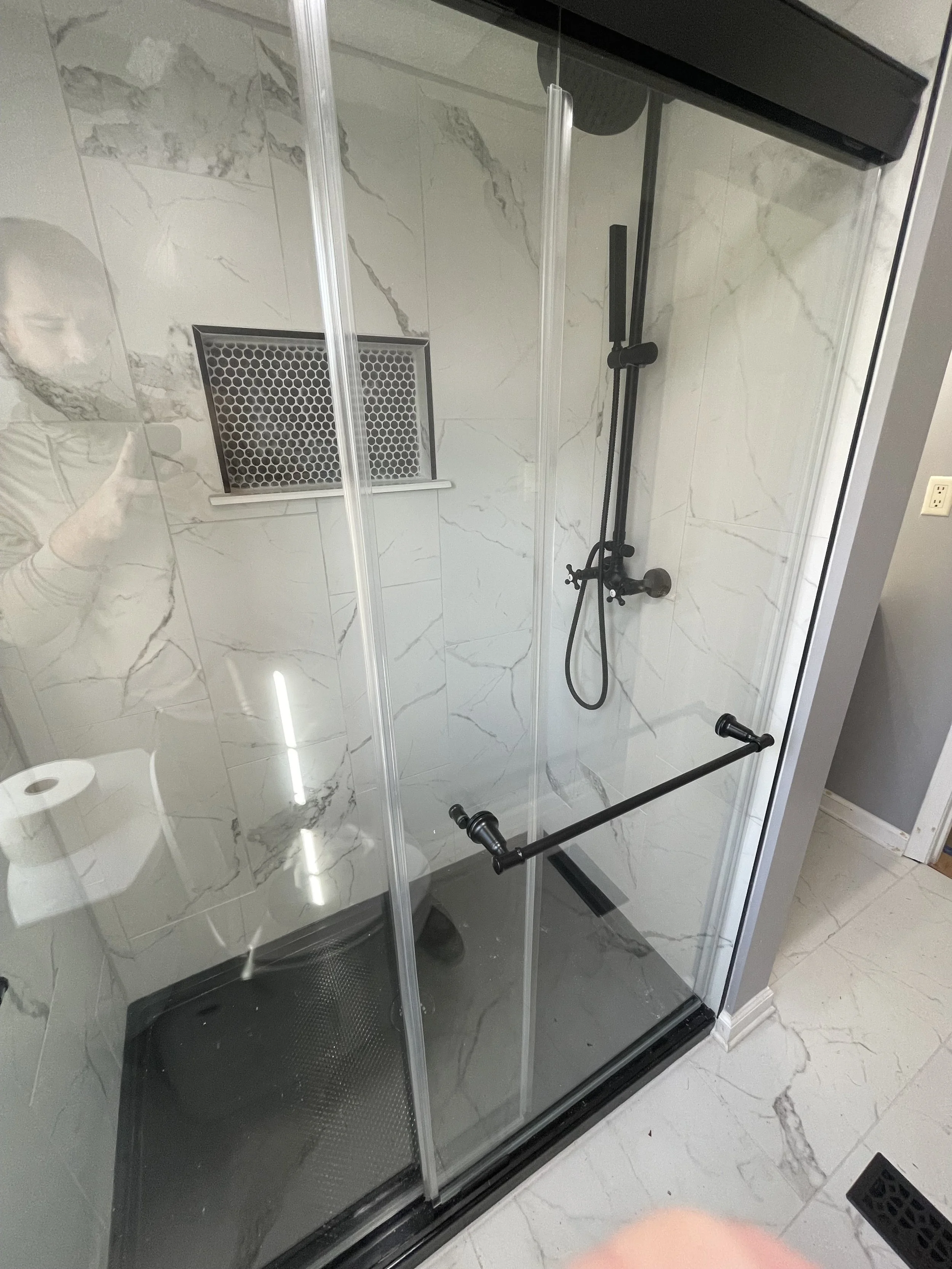 Shower with black fixtures, glass door, and marble wall tiles.