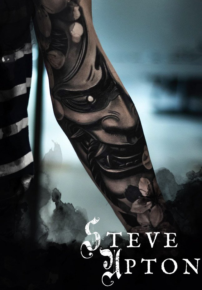 Close-up of a person’s black and grey tattooed arm featuring a detailed face and flowers from a Japanese theme. The image says "Steve Upton" at the bottom