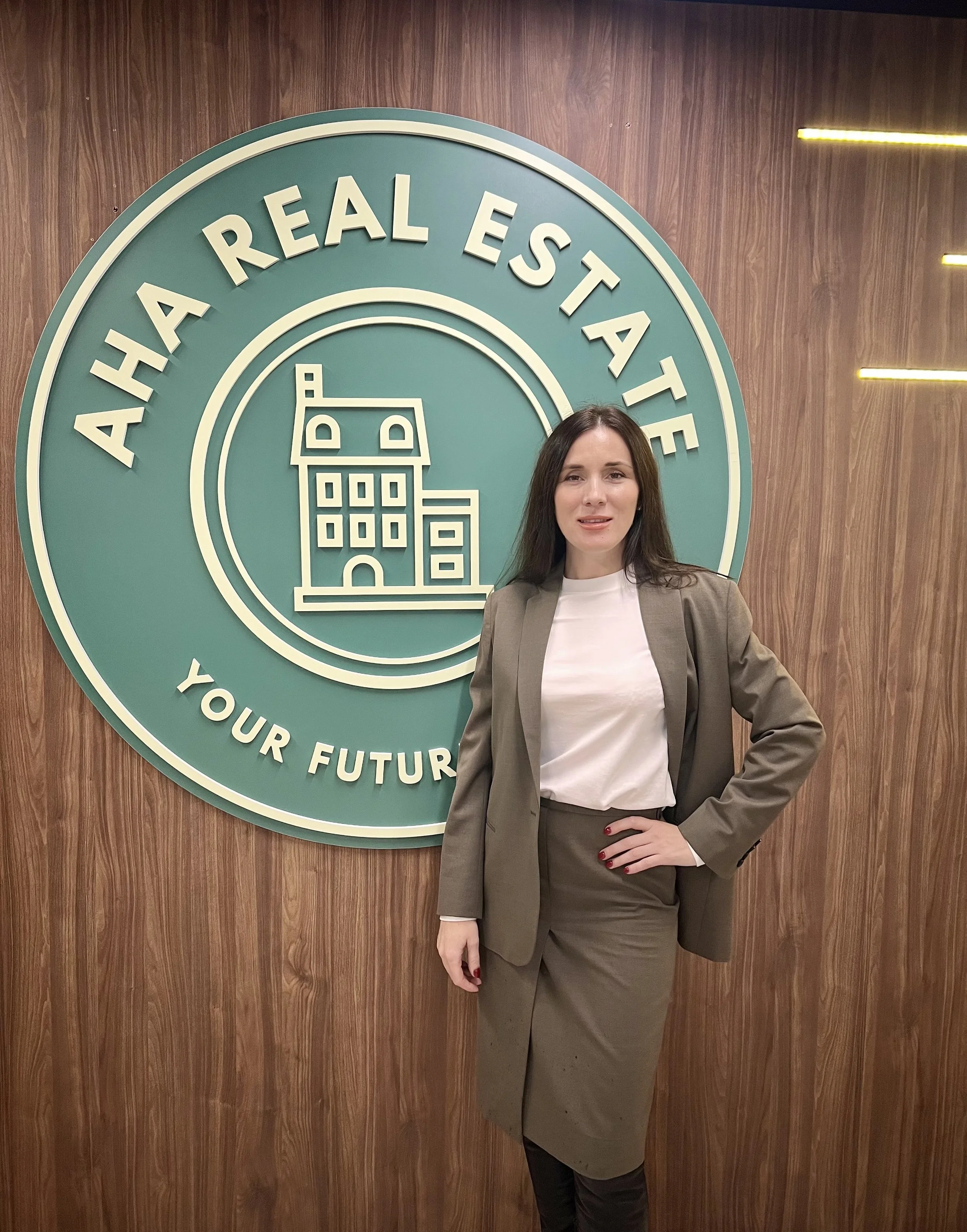 A woman in a business suit standing in front of a large circular sign that says 'Aha a real estate', with a building graphic and the slogan 'Your future'.