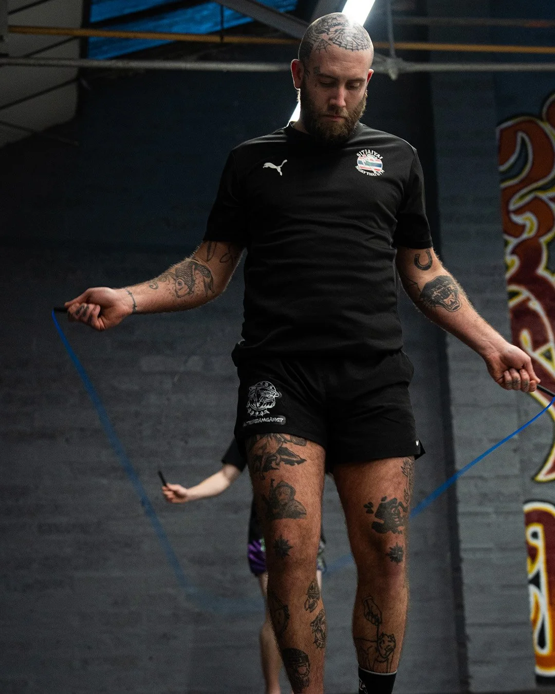 Man with tattoos skipping rope in a gym.