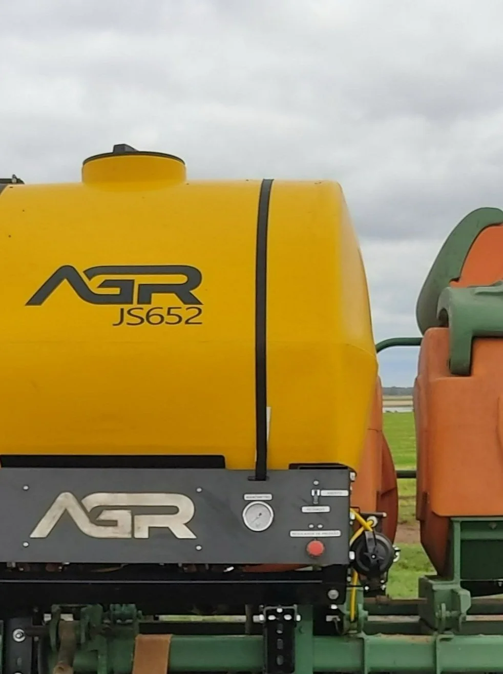 Imagem de uma máquina agrícola amarela, com o logo 'AGR' e o código 'JS652', ao ar livre, com céu nublado ao fundo.