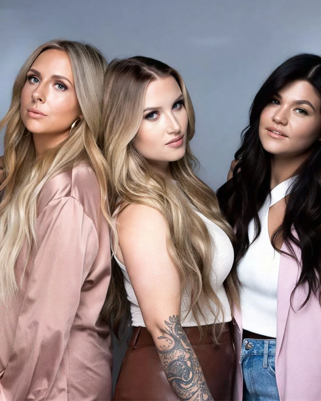 Three women with different hair colors and styles posing together against a neutral background.