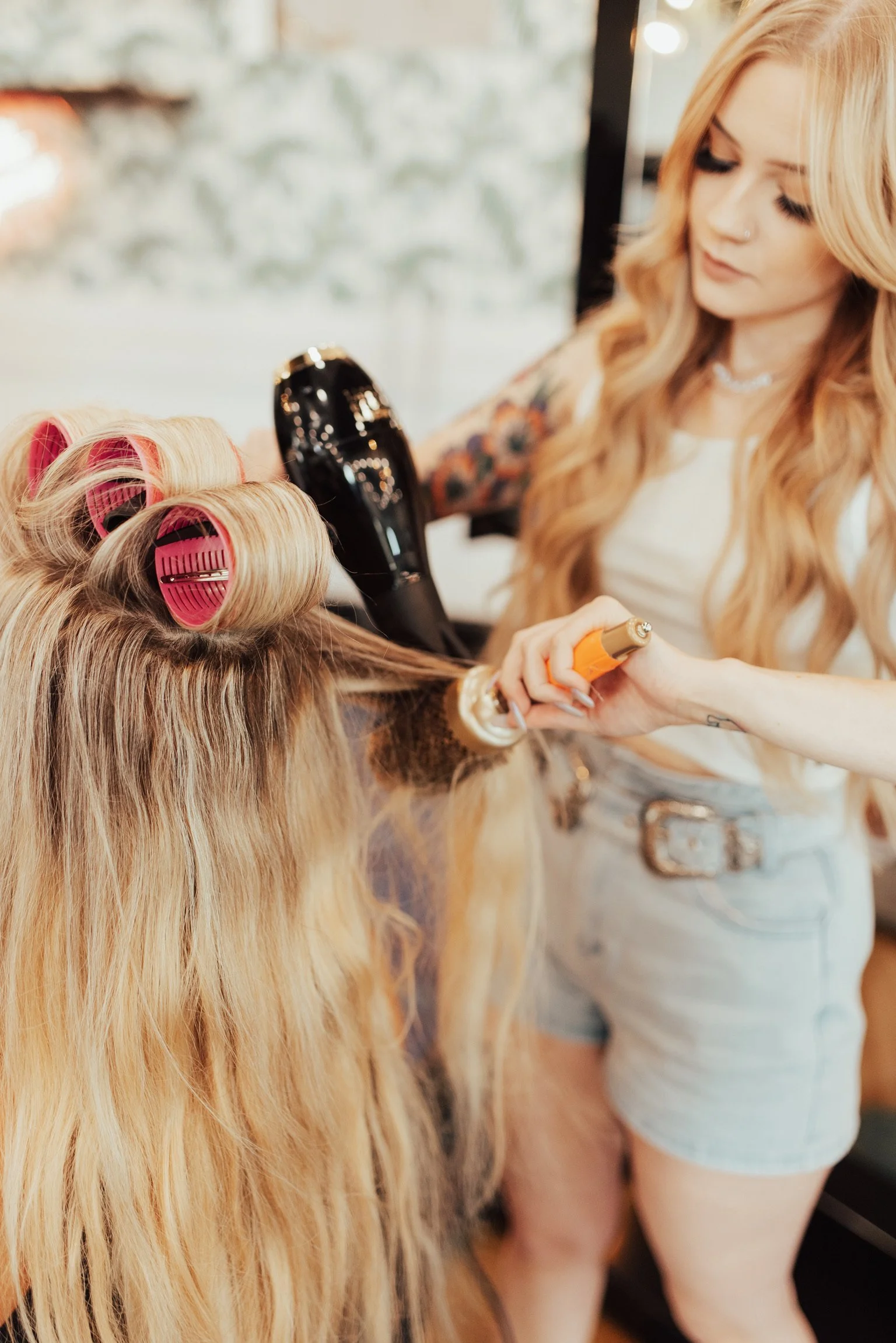 The stylist is blow-drying the client’s hair.