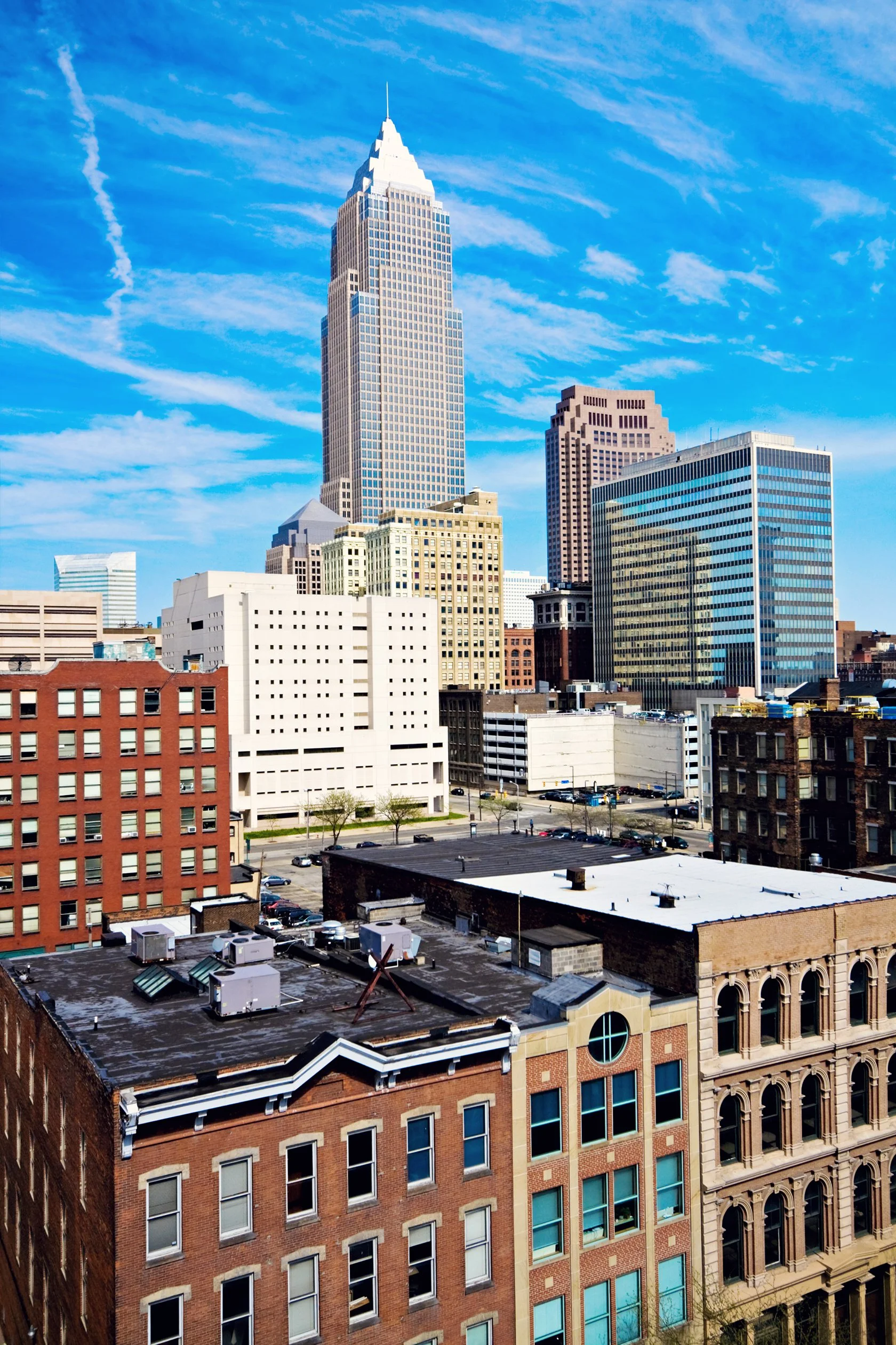 Skyline view of downtown buildings, including a tall, white and beige skyscraper against a blue sky with wispy clouds.