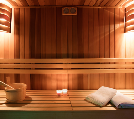 Interior of a wooden sauna with a bench, two candles, a towel, and a bucket with a ladle inside.