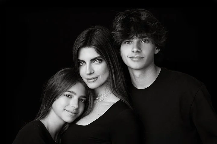 Black and white portrait of a woman with long hair and two teenagers, one girl on her left and boy on her right, all smiling gently at the camera.