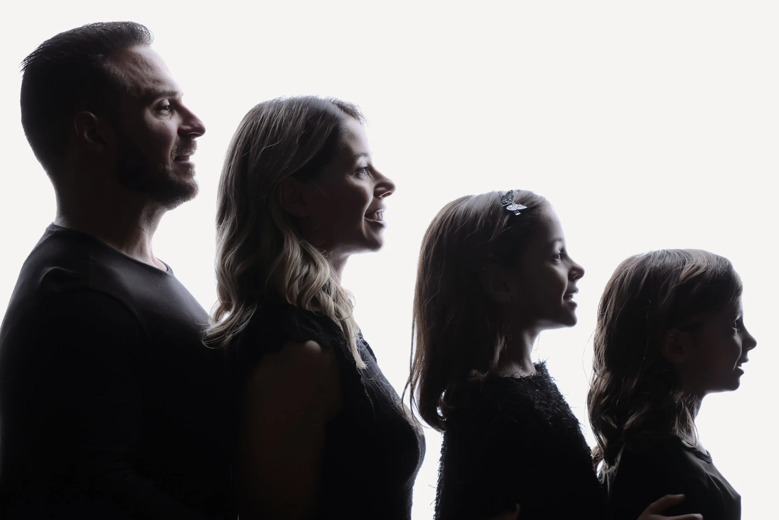 A silhouette of a family of five standing in a line, facing right, with bright light behind them. The family includes two adult males and three females of varying ages.