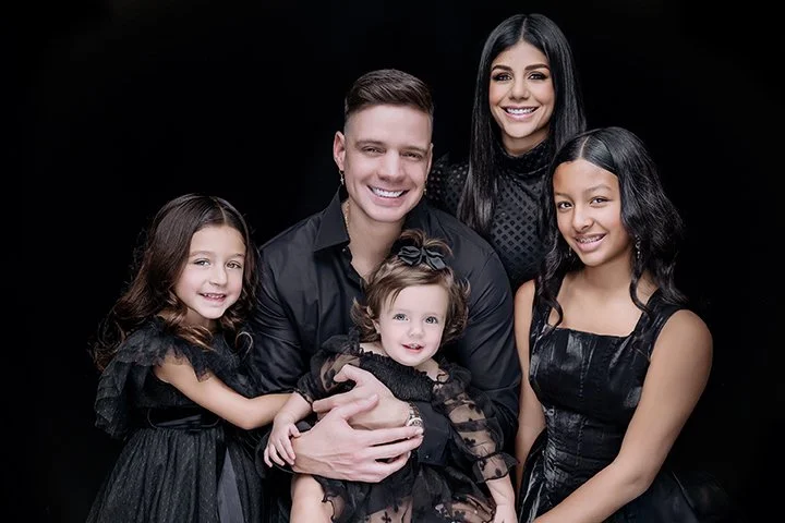 Group portrait of a smiling family of five dressed in black against a black background.