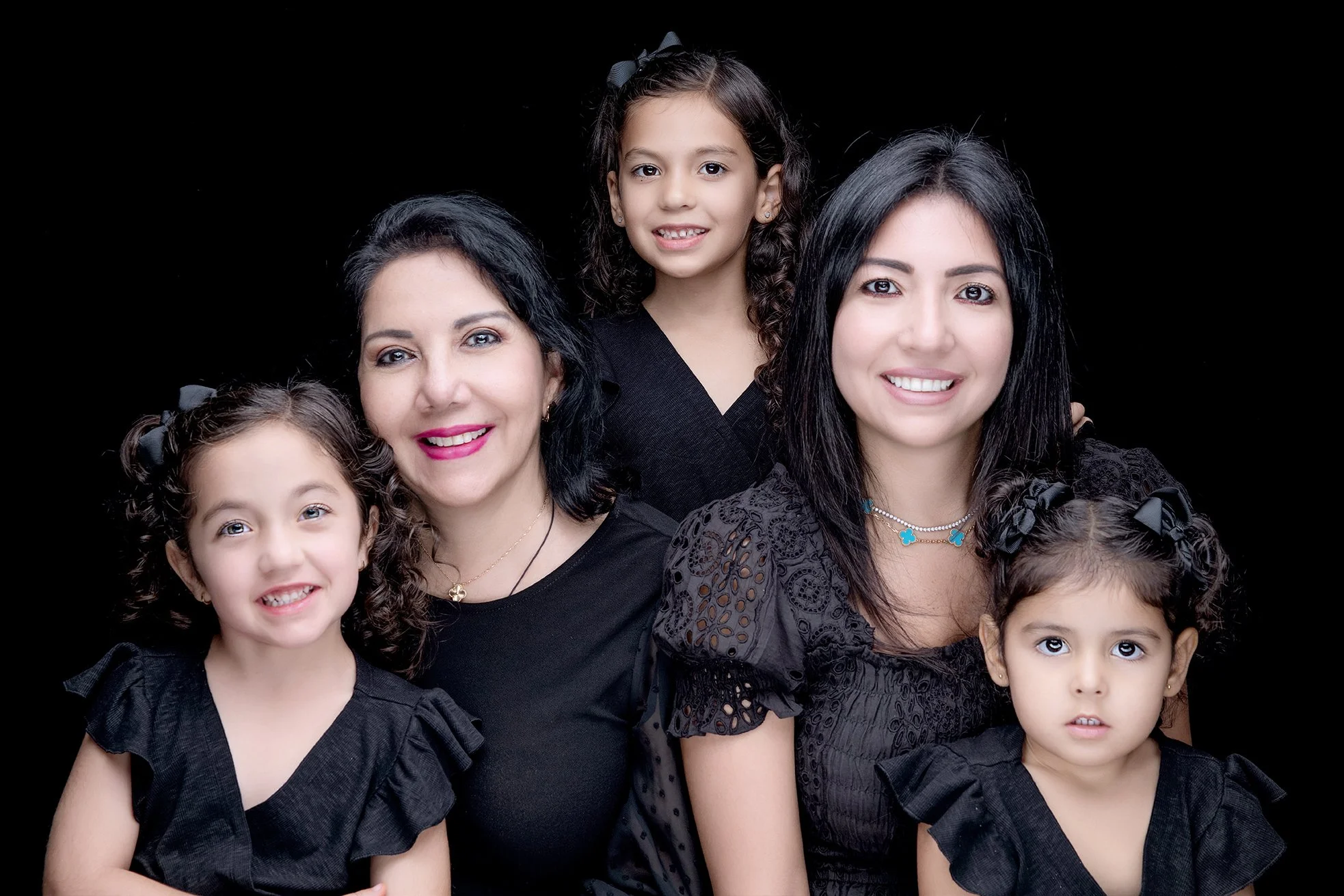 A family portrait of five women and girls, all wearing black tops, smiling against a black background.