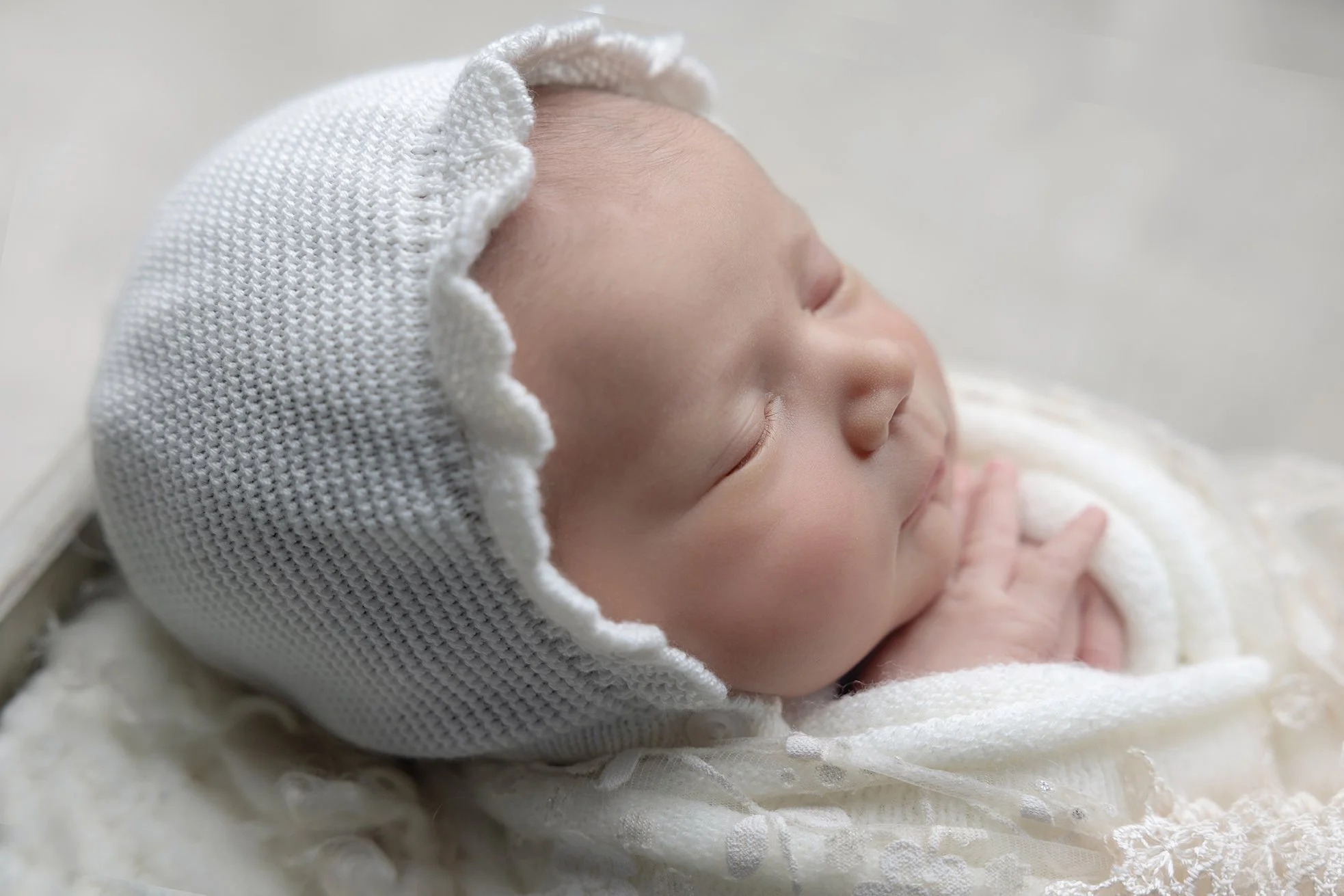 Close-up of a sleeping newborn baby with a knit bonnet and soft clothing.